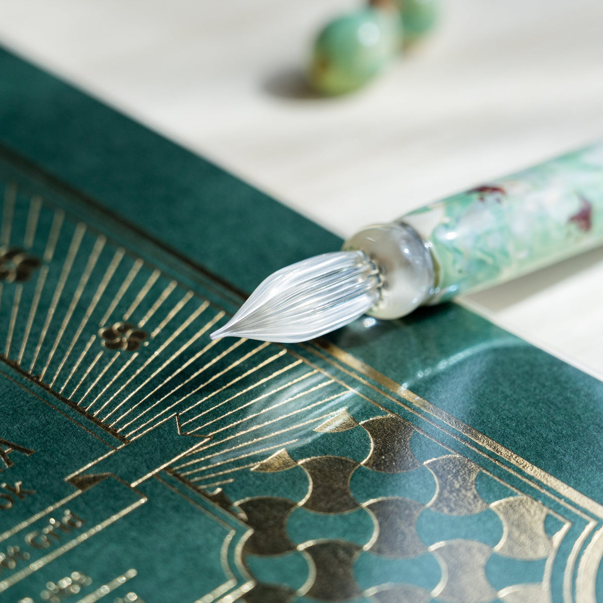 Clear fluted nib of the Chidori Mint Marble glass dip pen over a green gold foil notebook cover