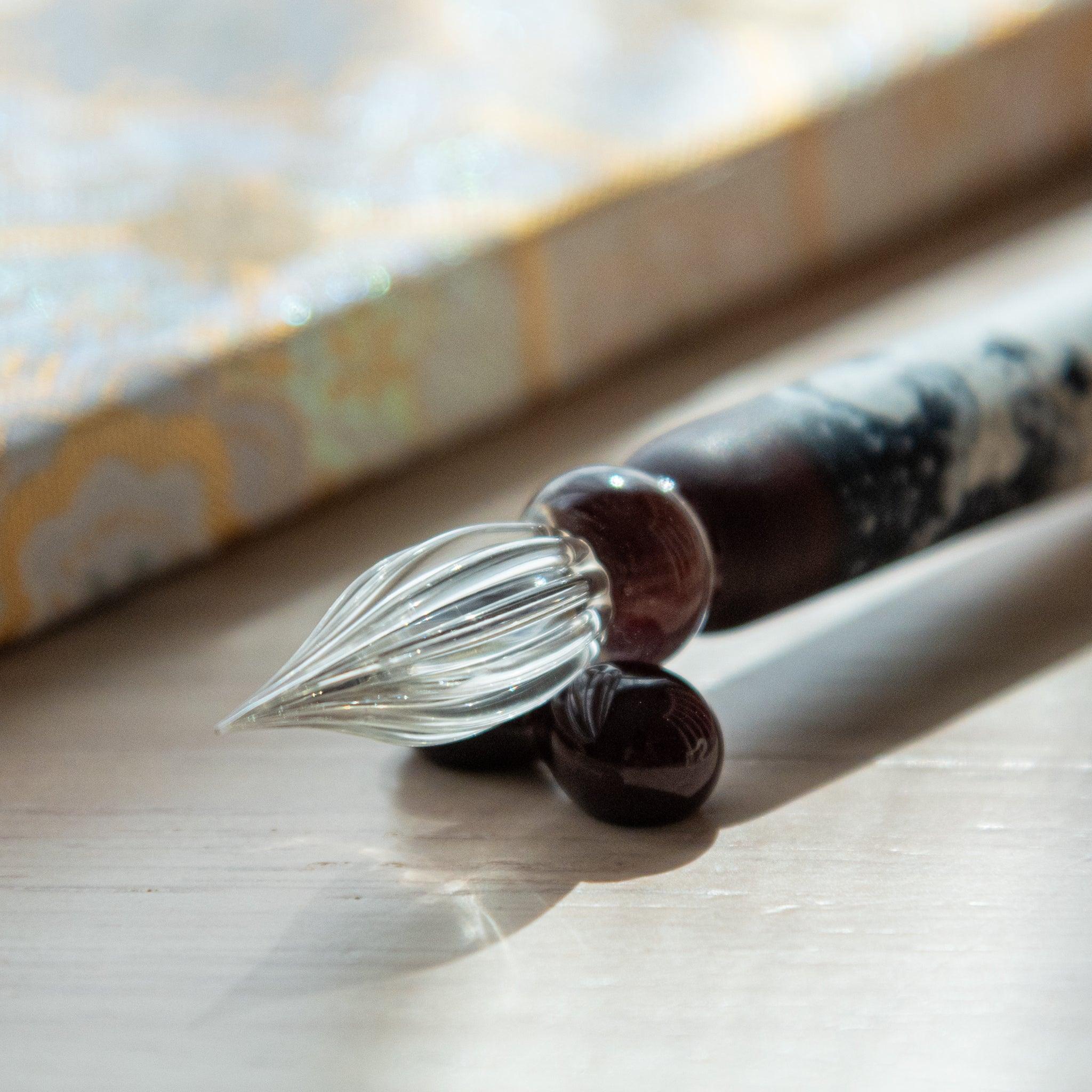 Black and white glass pen with a Chidori on Great Wave design, paired with a matching glass pen rest. Displayed on a wooden surface with a Nishijin textile notebook.