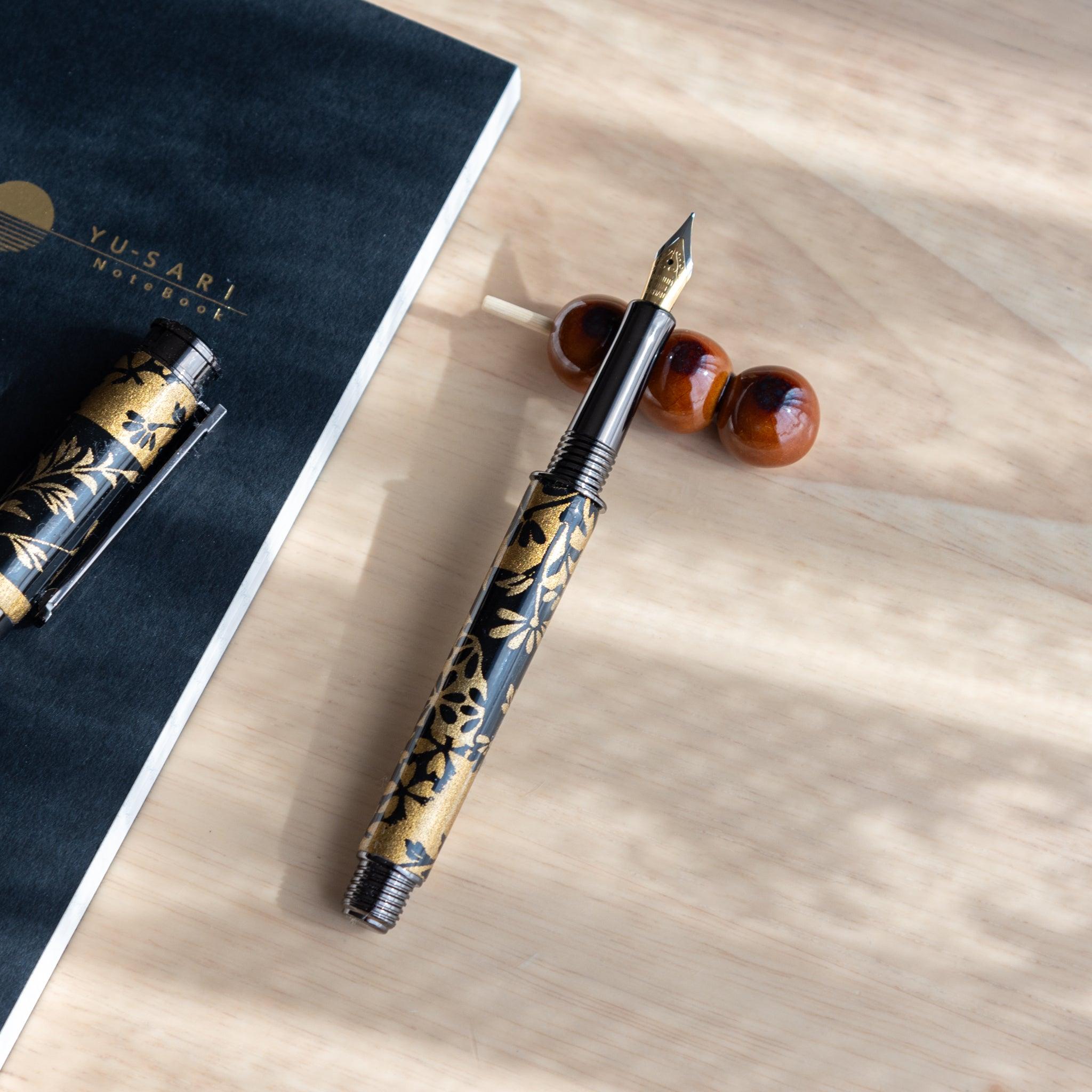 A handmade ceramic pen rest shaped as a mugwort dango skewer, holding a black and gold fountain pen. Part of traditional Japanese stationery items.