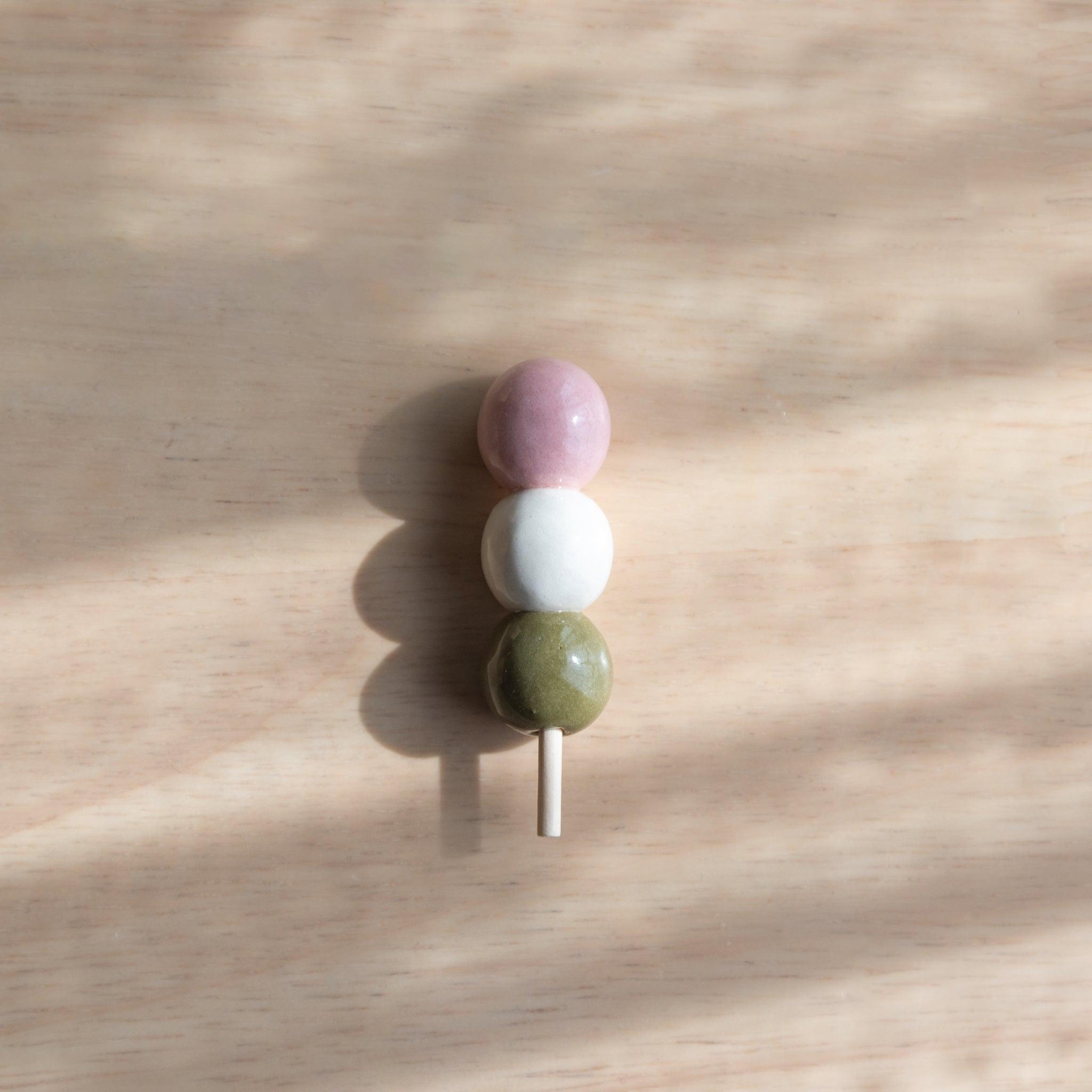 A handmade ceramic pen rest shaped as a hanami dango skewer, showcasing Japanese stationery craftsmanship with a seasonal and playful design.