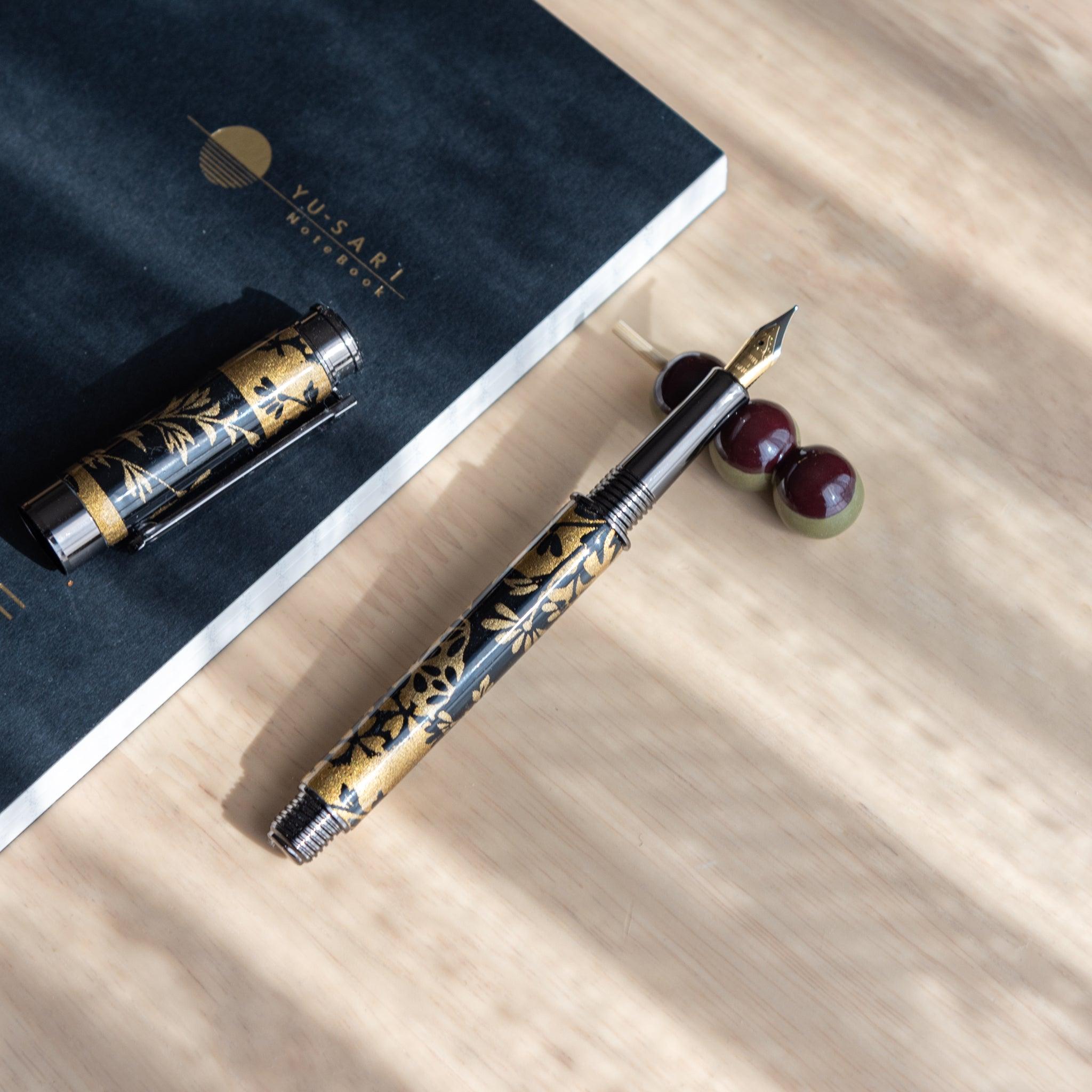 A handmade ceramic pen rest shaped as a mugwort dango skewer, holding a black and gold fountain pen. Part of traditional Japanese stationery items.