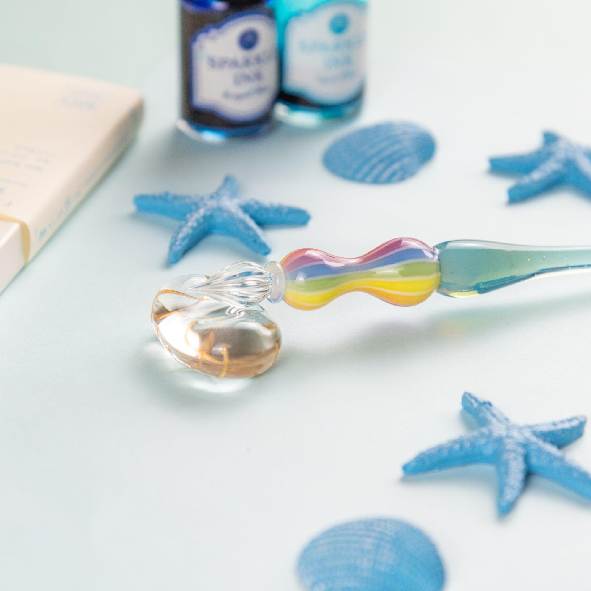 Hand holding a rainbow-colored glass pen, writing on an open notebook. Ideal for glass pen lovers and fans of Japanese stationery.