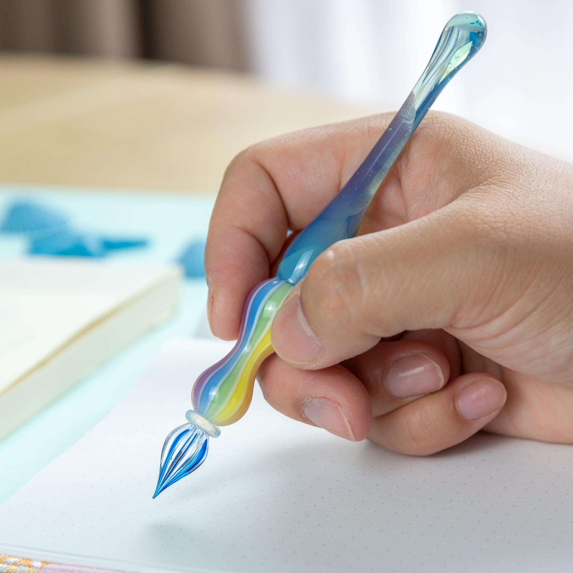 Rainbow balloon glass pen resting on a clear pen rest, surrounded by blue starfish and seashells. Perfect for Japanese stationery lovers.