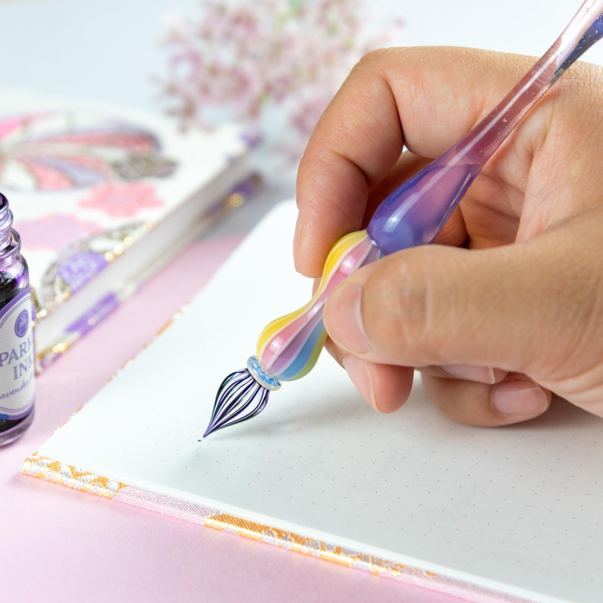 Pastel purple glass pen with rainbow-striped handle, resting on an open notebook with Japanese fabric cover. Ideal for Japanese stationery and glass pen lovers.