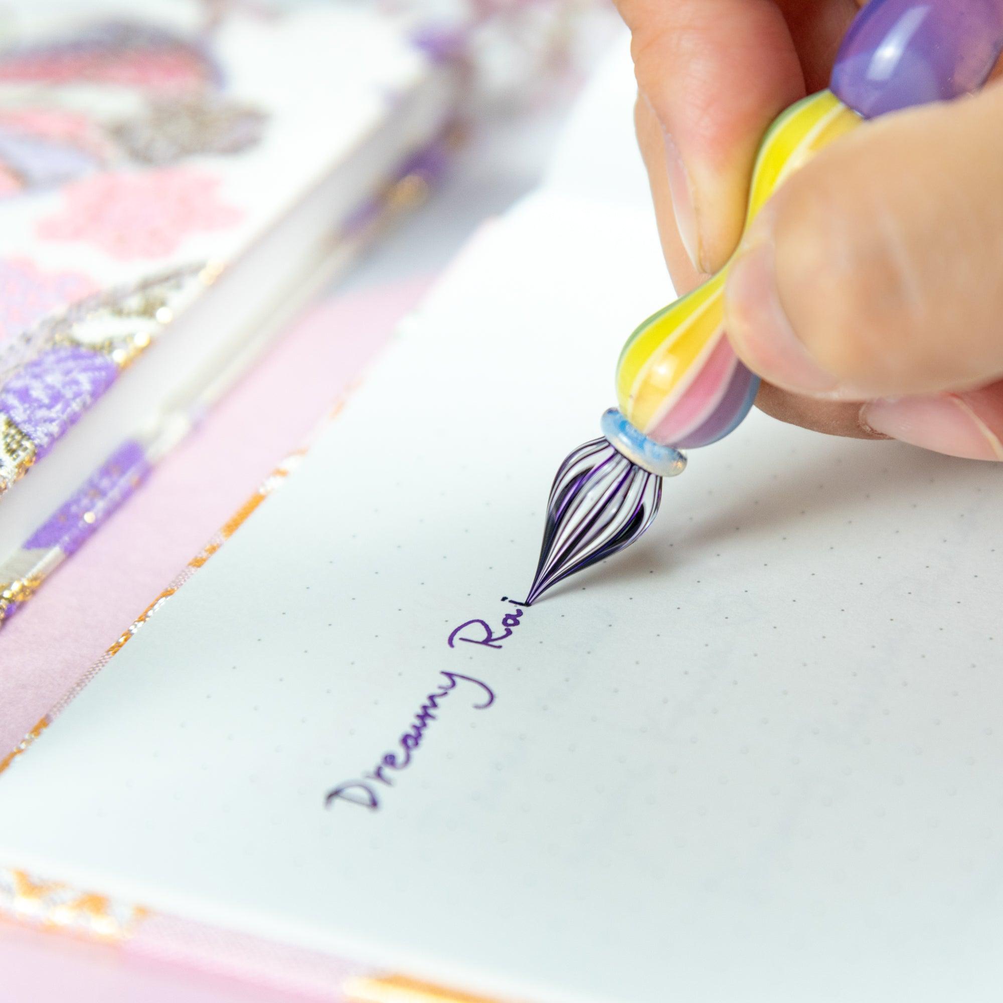 Pastel purple glass pen with rainbow-striped handle on a notebook with Japanese fabric cover. Perfect for glass pen and Japanese stationery enthusiasts.