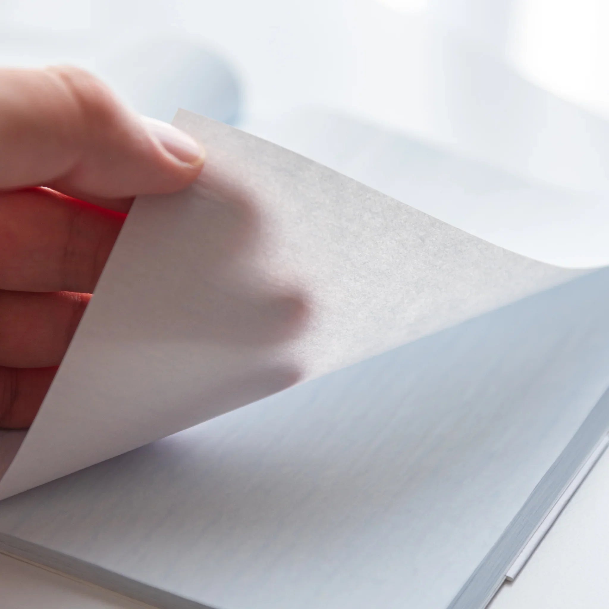 Hand flipping the delicate pale blue page of Dressco Blue Onion Skin Japanese Notebook B6, showing translucency.