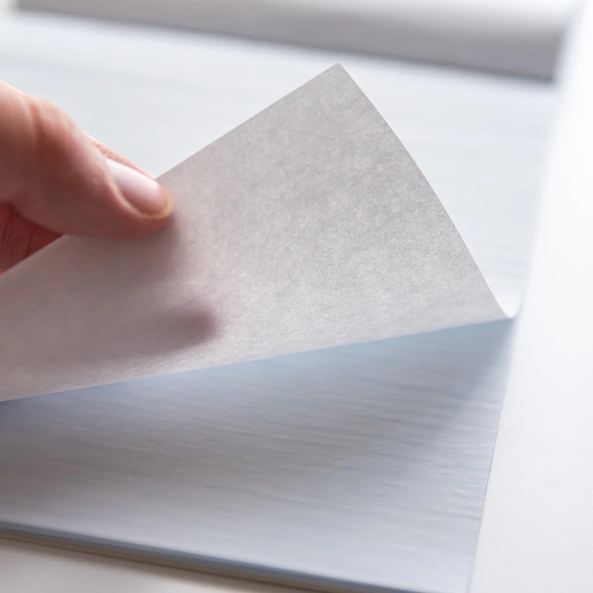 Close-up of thin translucent sheet from Dressco Blue Onion Skin Japanese Paper Writing Pad being lifted by hand.