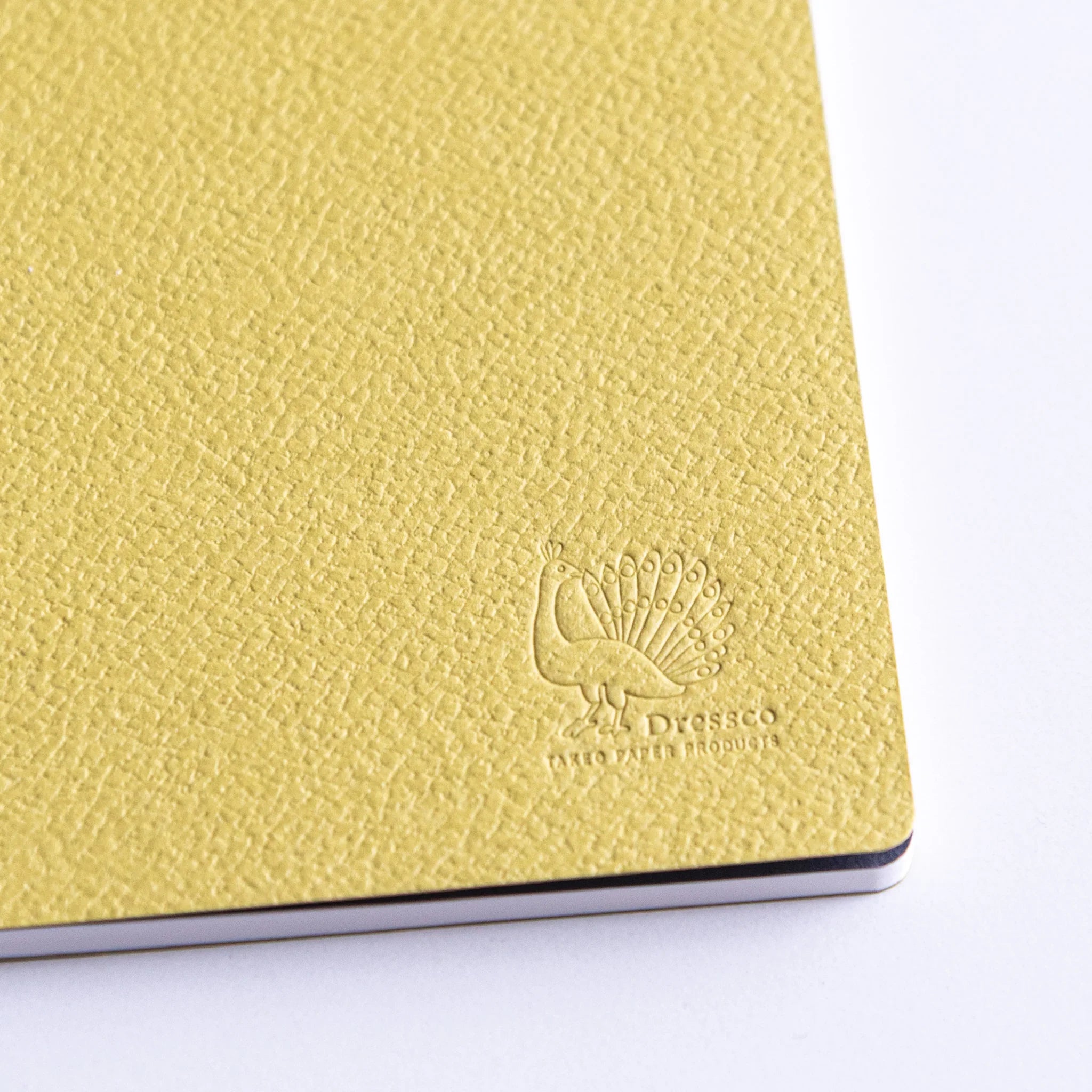 Close-up of Dressco peacock logo embossed on Avocado Spica Laid Bond Japanese Notebook.