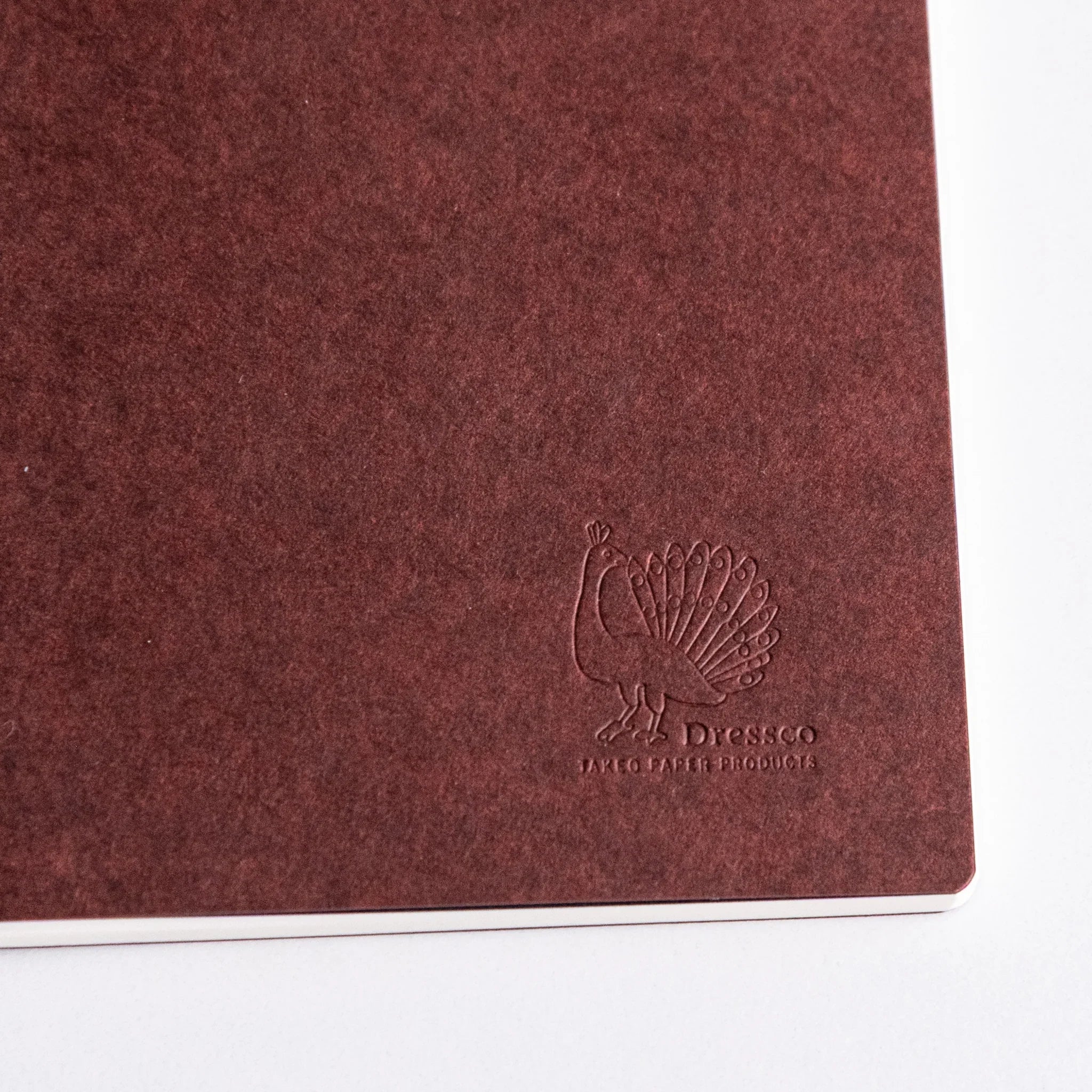 Close-up of maroon Japanese notebook cover with embossed peacock logo made from Bank Ledger Paper.