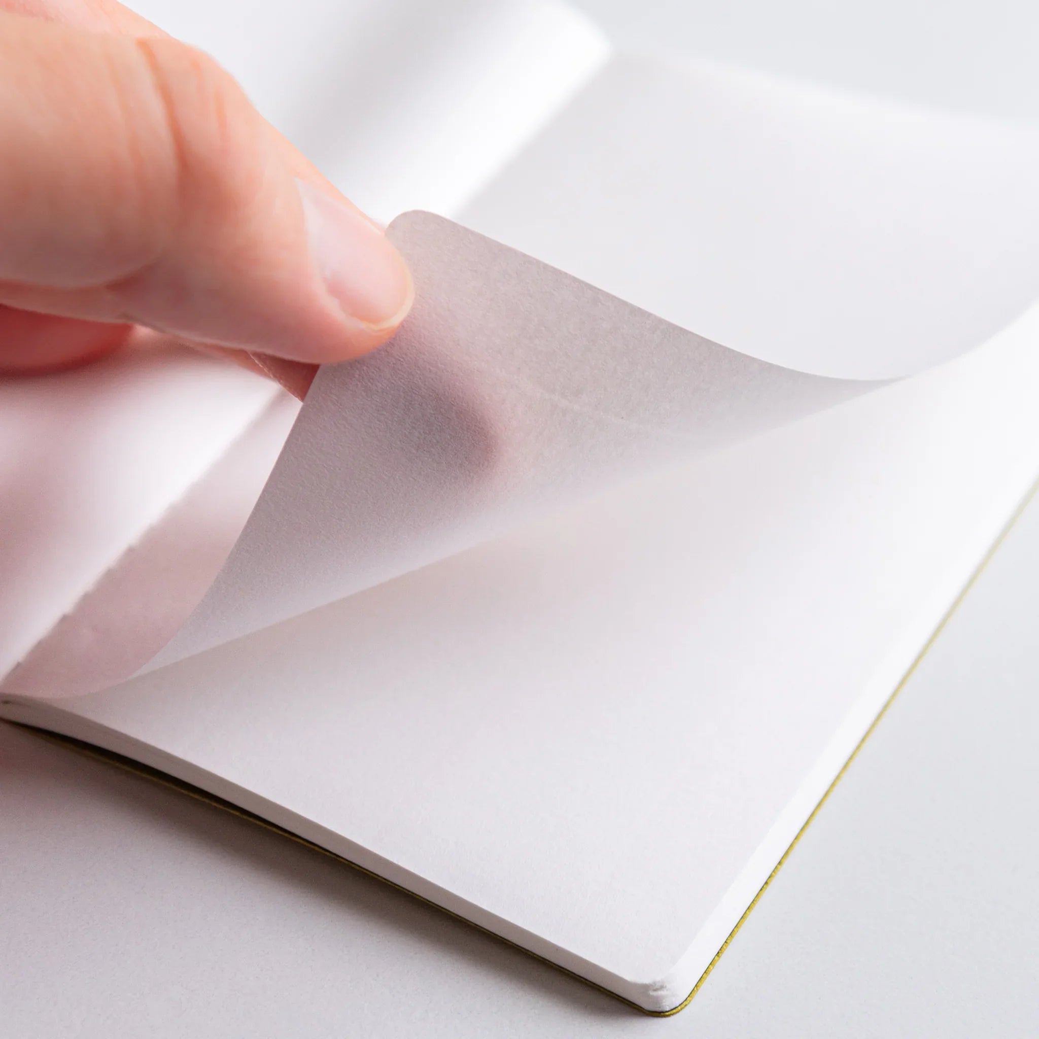 Close-up of Spica Laid Bond Paper Japanese notebook, showing hand turning a delicate translucent page with stitched binding.