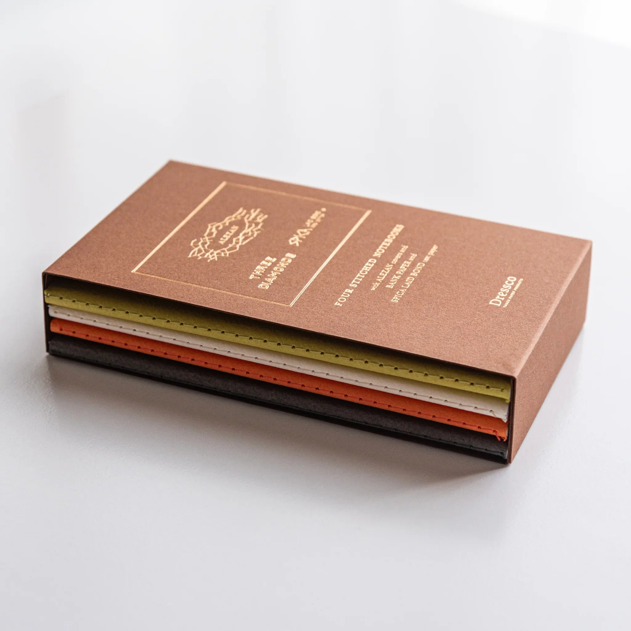 Elegant Japanese notebook set of four presented in an Alezan book case, showcasing a stack of colorful stitched notebooks.
