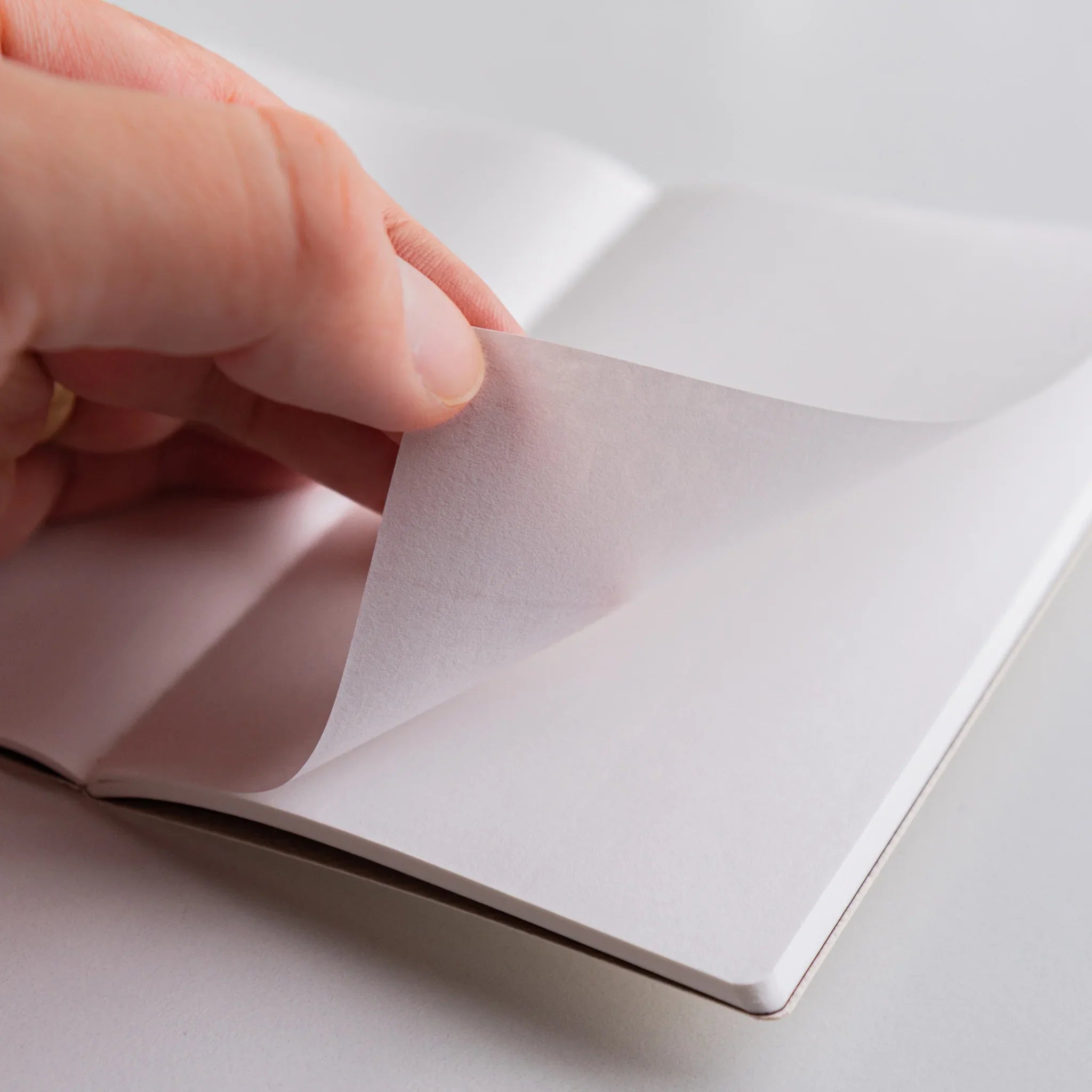 Close-up of hand lifting a delicate page of Spica Laid Bond Paper Japanese notebook, highlighting thin translucent sheet and tactile quality.