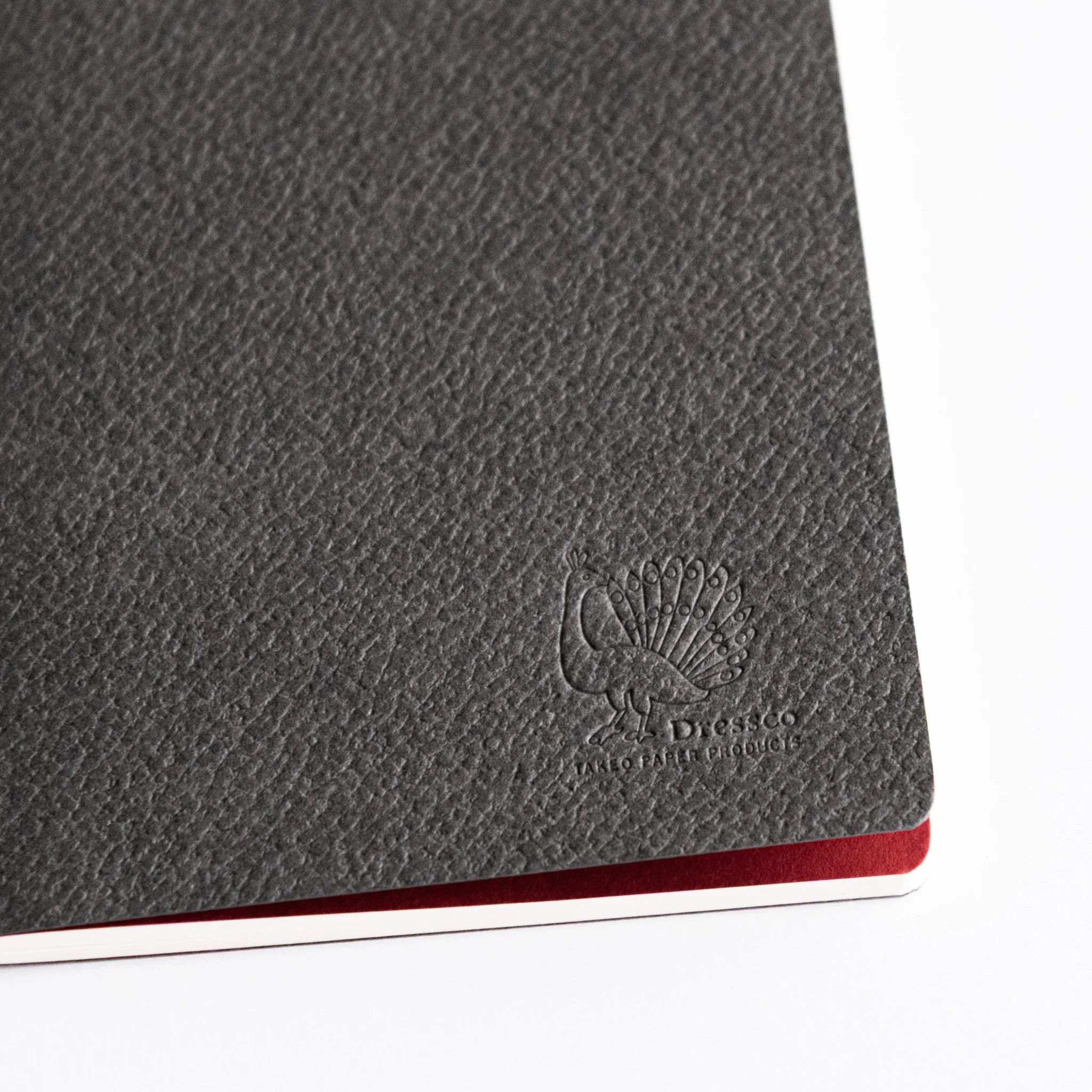 Close-up of Bank Ledger Paper Japanese notebook cover showing textured dark gray surface and embossed Dressco peacock logo.