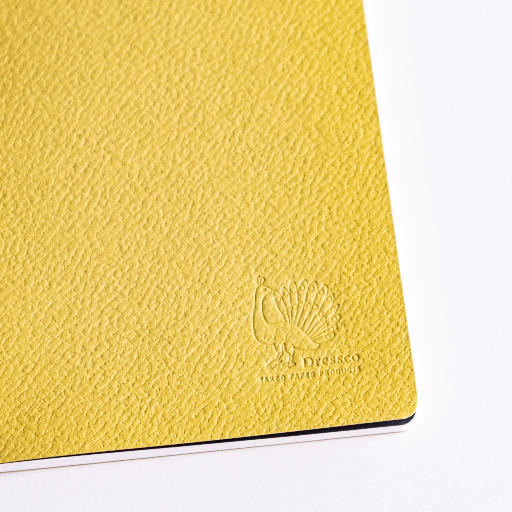 Close-up of Spica Laid Bond Paper Japanese notebook cover in avocado color, showing textured surface and embossed Dressco logo.