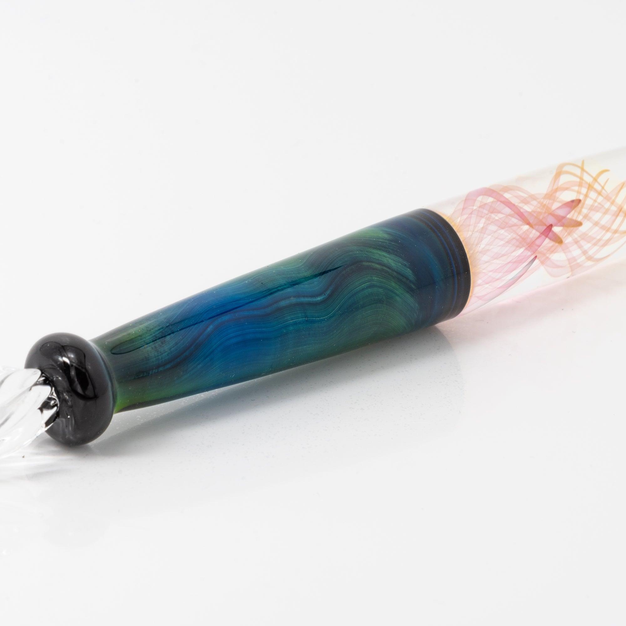 A glass pen with a blue and green body featuring swirling patterns, lying on a white background. The nib is delicately shaped for writing.