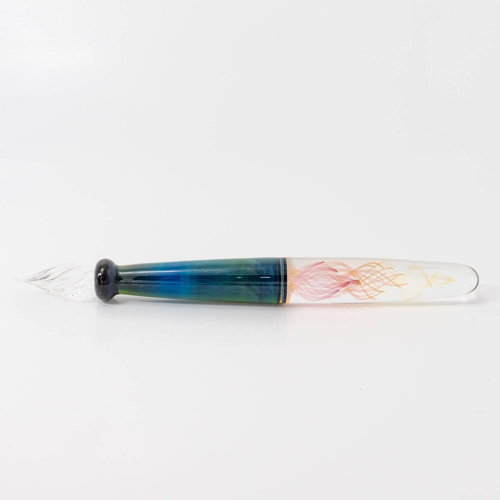 A glass pen with a blue and green body featuring swirling patterns, lying on a white background. The nib is delicately shaped for writing.