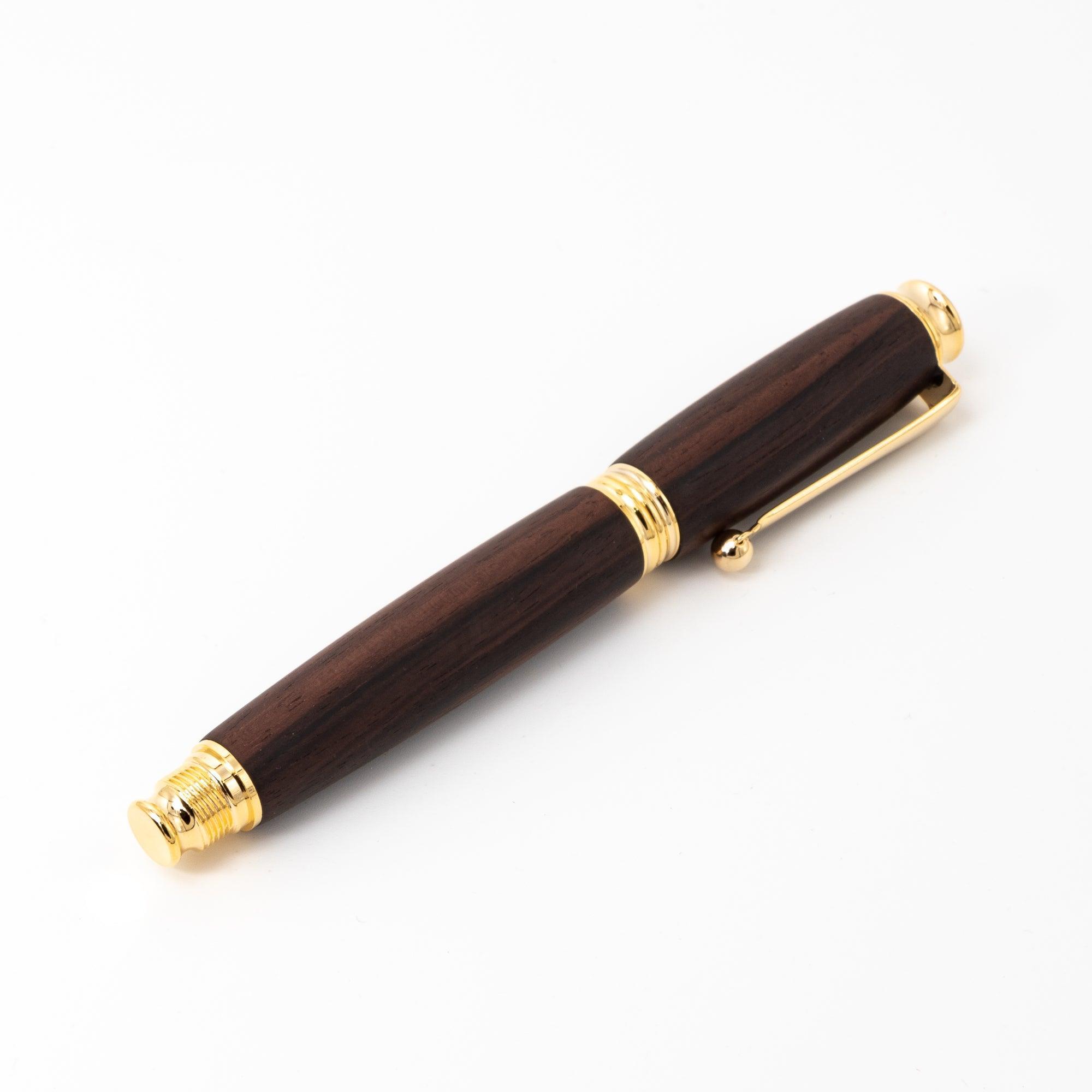 A Japanese fountain pen made of dark ebony wood with gold trims, displayed horizontally against a plain white background for a minimalist presentation.