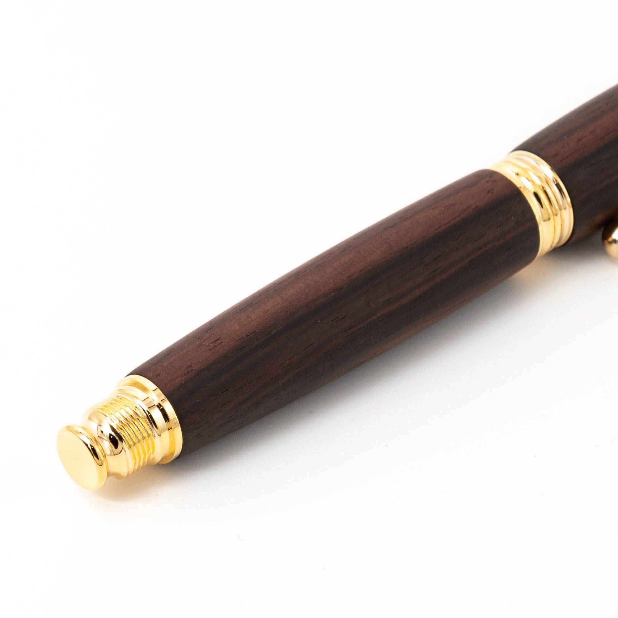 A detailed view of a Japanese fountain pen’s wooden barrel and gold screw cap, emphasizing the dark ebony grain against a plain background.