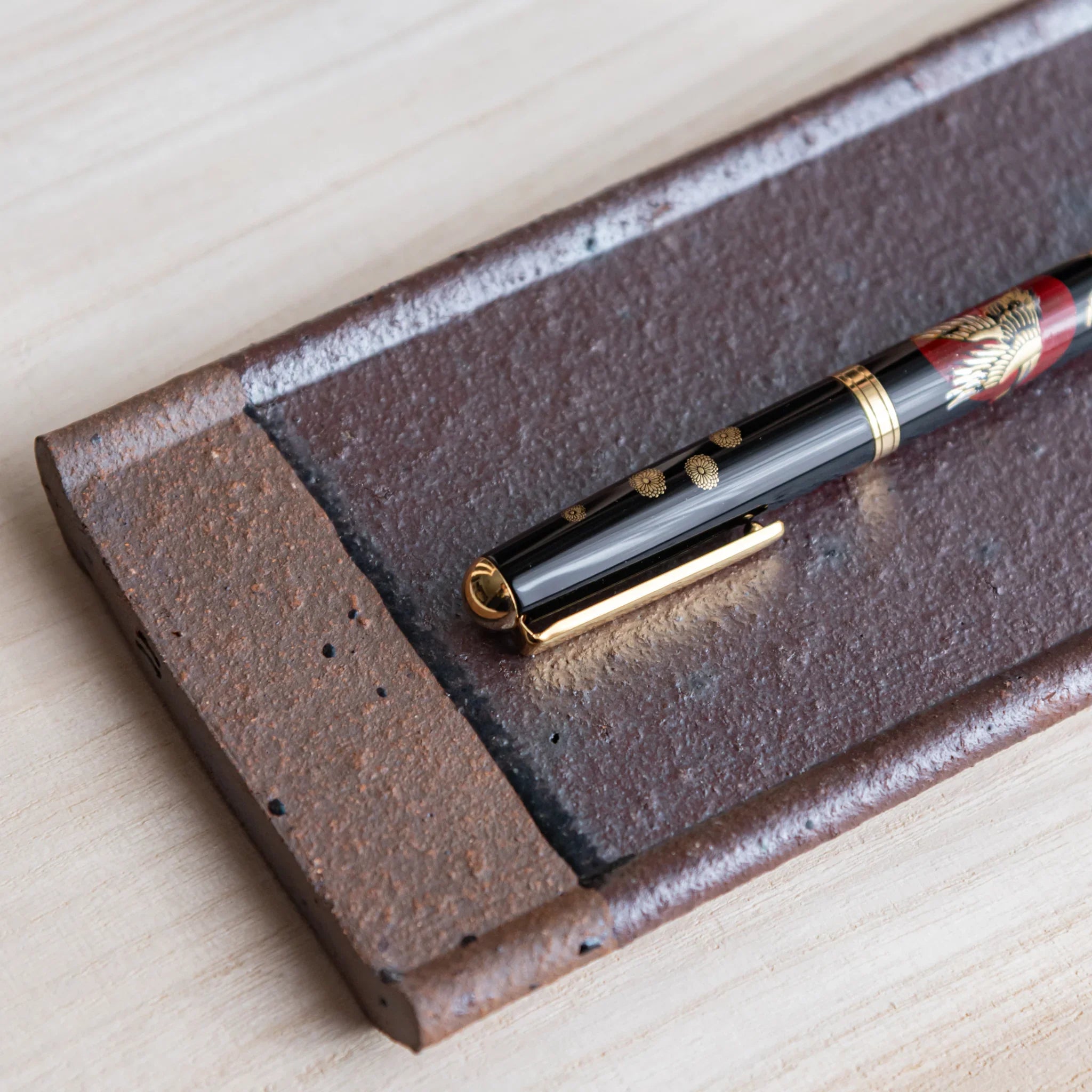 Japanese Pen Tray Desk Accessory featuring angled view of red ceramic tray with fountain pen placed diagonally on it.