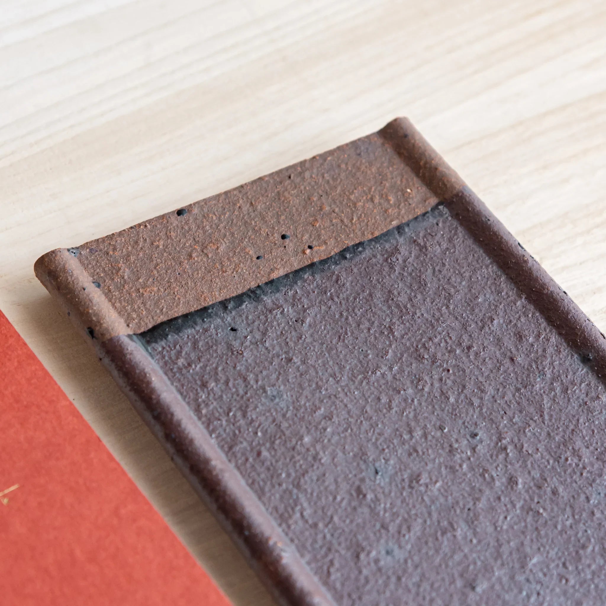 Japanese Pen Tray Desk Accessory showing close-up angled view of red ceramic tray with brown end on light wooden surface.
