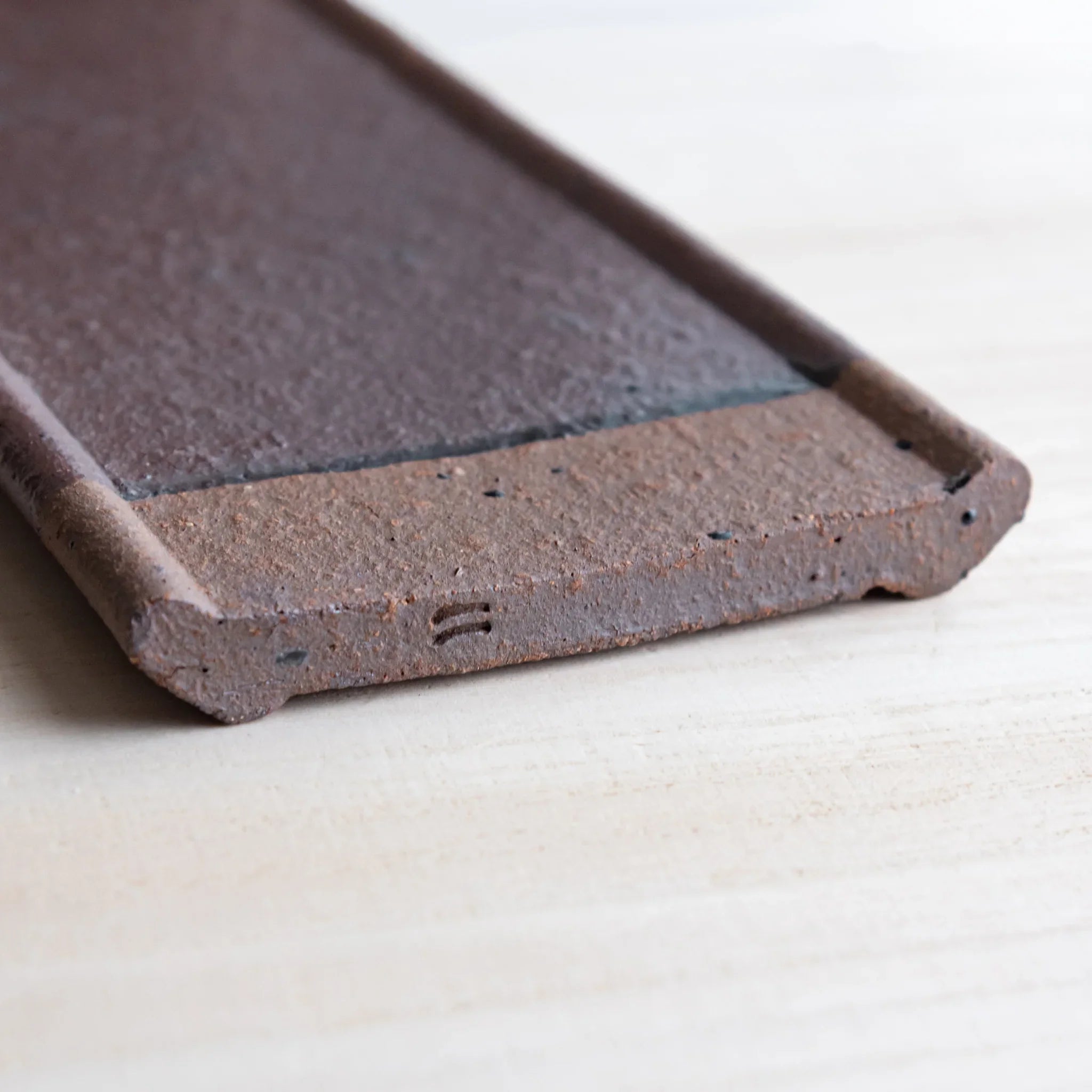 Japanese Pen Tray Desk Accessory angled view of red ceramic tray showing grooves and raised edges on light wooden surface.