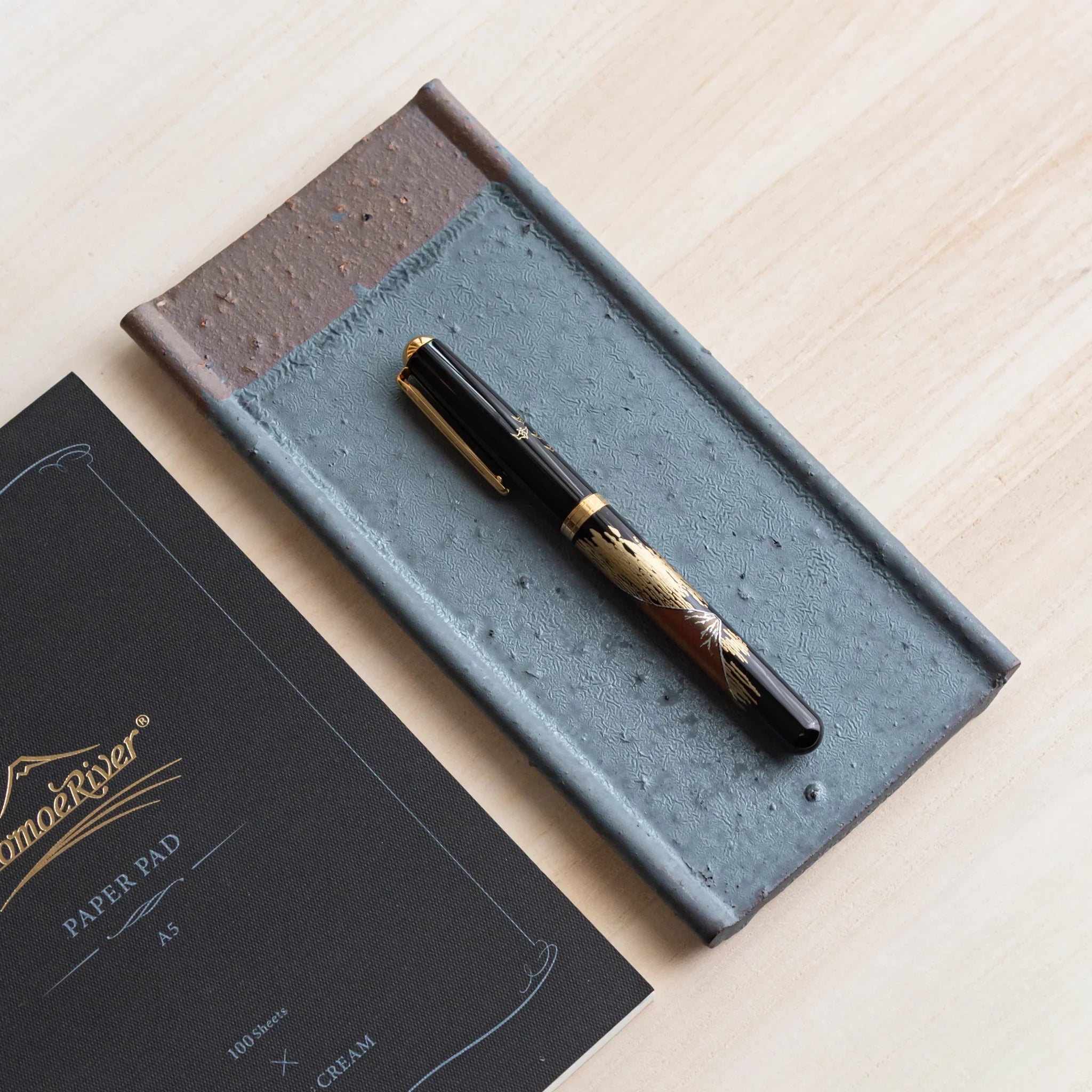 Japanese Pen Tray Desk Accessory with silver gray ceramic tray holding a fountain pen next to Tomoe River notebook.