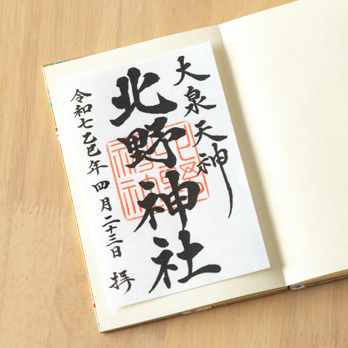 Washi goshuincho stamp book open to an ivory page with a goshuin sheet, black brush calligraphy and red shrine seals