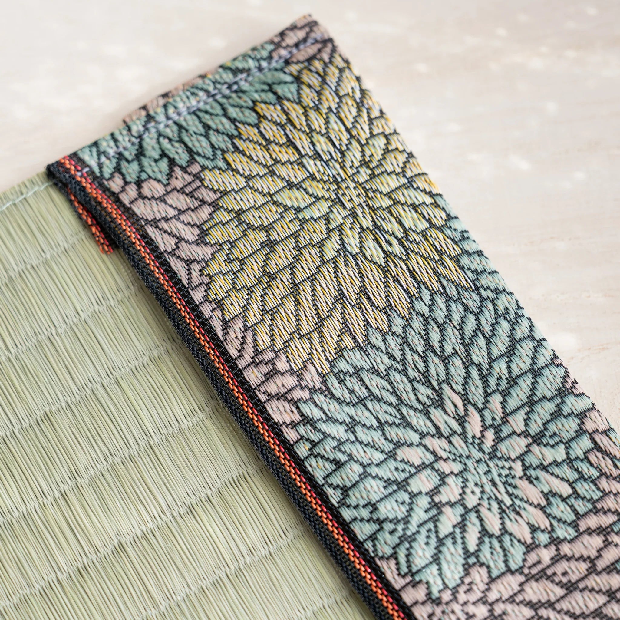 Close-up of Japanese chrysanthemum brocade band in green pink and yellow with orange striped trim beside rush straw