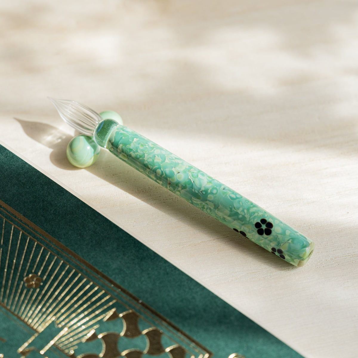 Emerald Flower glass dip pen angled on pale wood, green marbled barrel with dark blossom motifs
