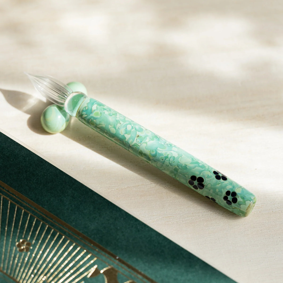 Emerald Flower glass dip pen with green marbled barrel and black blossom motifs beside a green glass pen rest