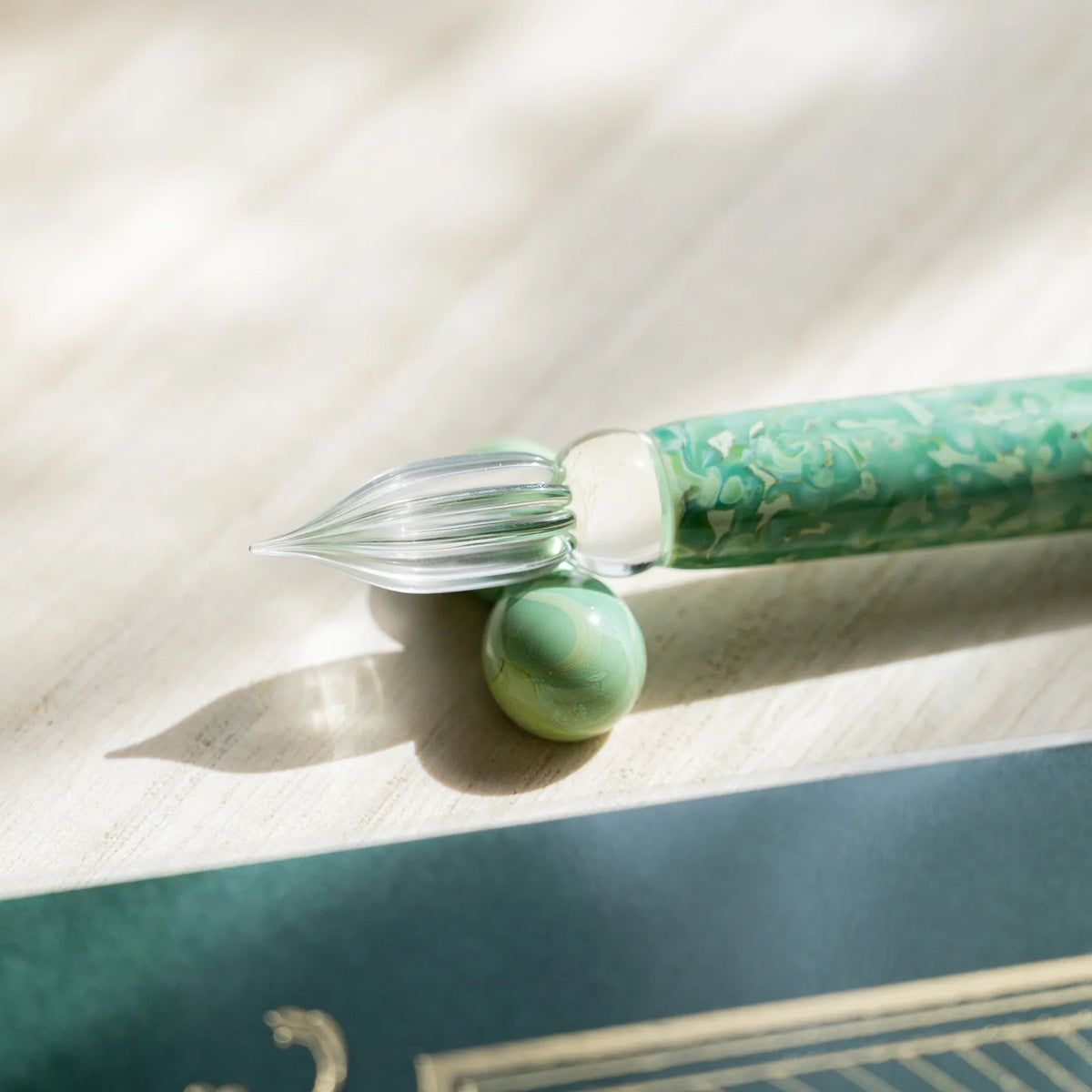 Emerald Flower glass dip pen nib tilted onto a green marbled glass sphere pen rest