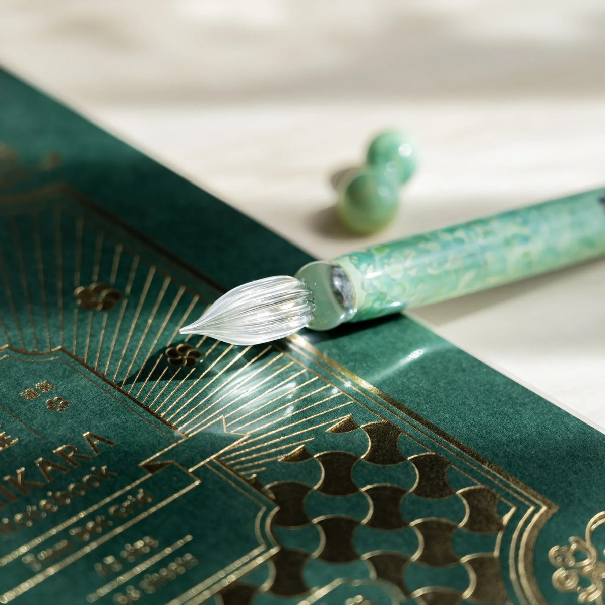 Clear fluted nib of the Emerald Flower glass dip pen over a green gold foil notebook cover