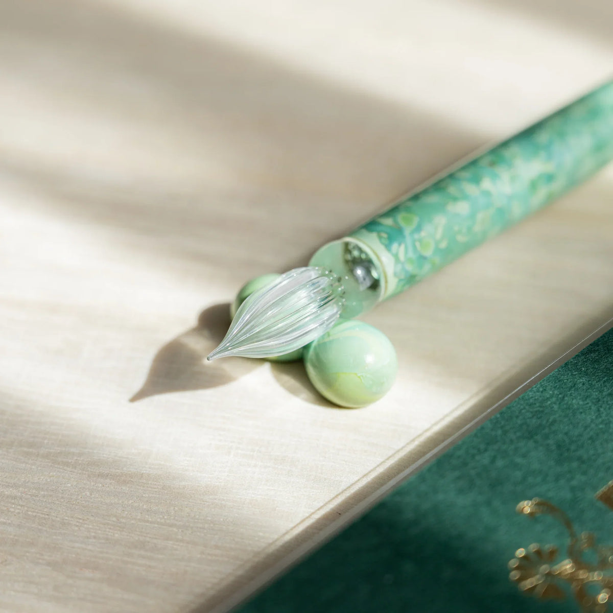 Clear ribbed nib and green marbled barrel of the Emerald Flower pen resting on a glass sphere
