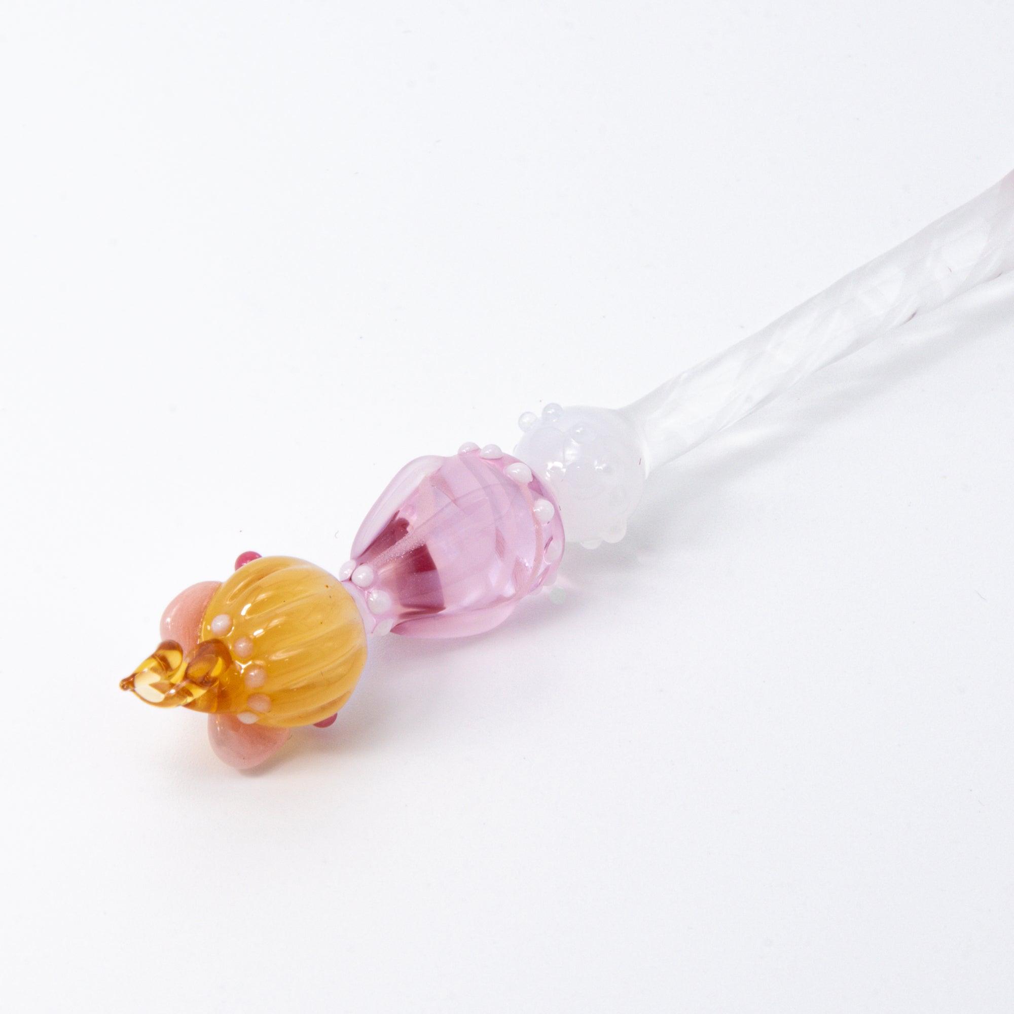 A top view of a Lovery-chan glass pen with a heart design, featuring a cute figure on top, dressed in pink with hearts along the pen shaft.