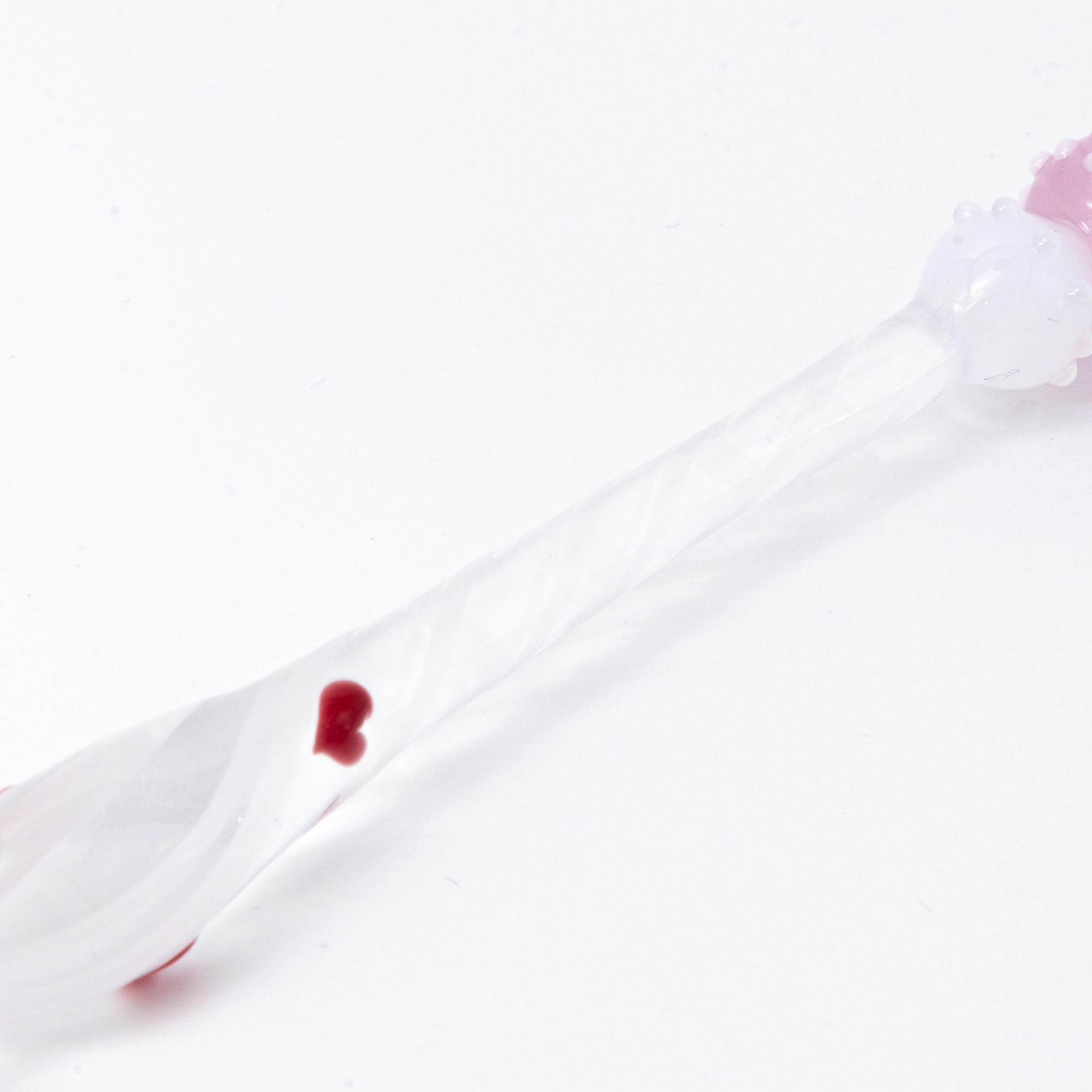 A top view of a Lovery-chan glass pen with a heart design, featuring a cute figure on top, dressed in pink with hearts along the pen shaft.