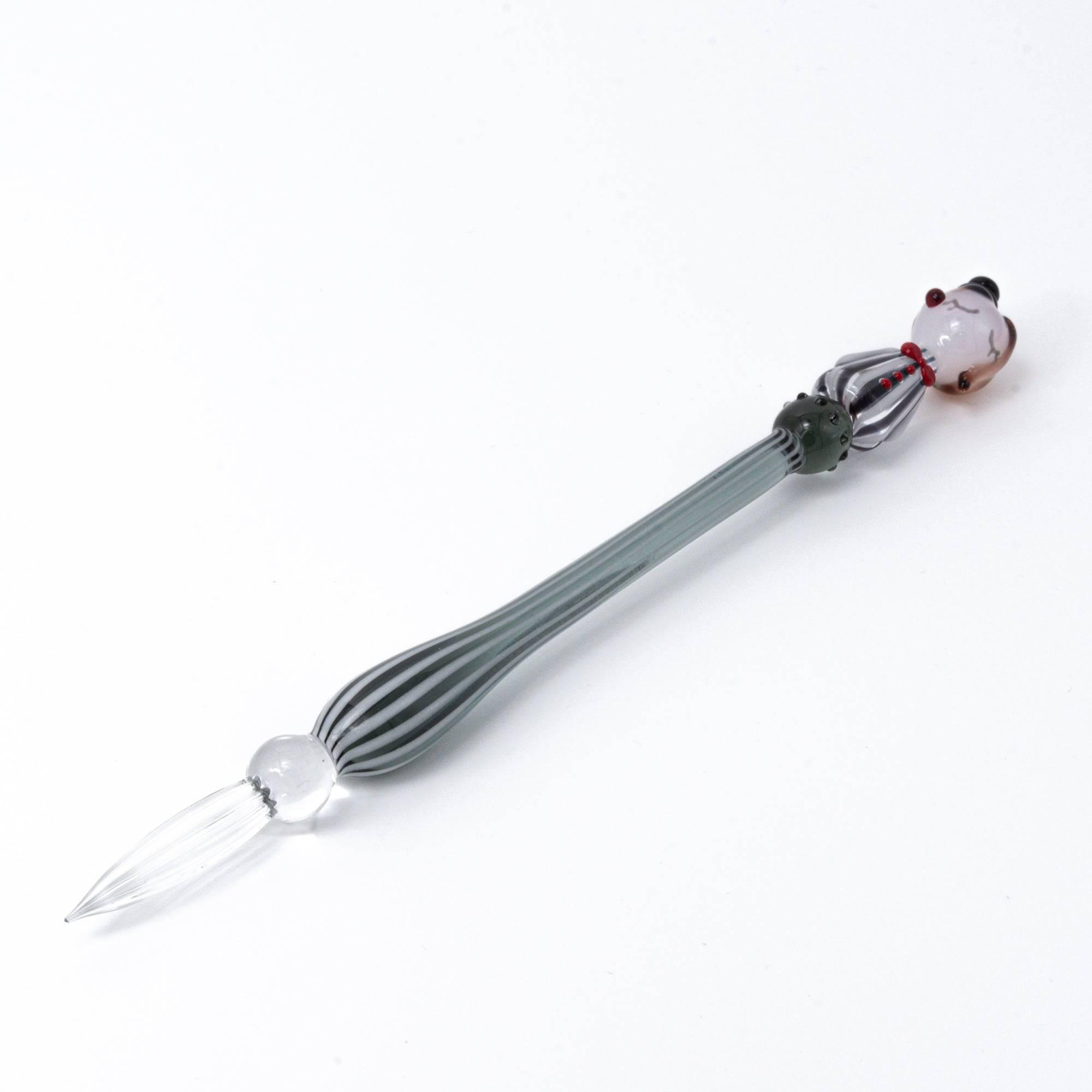 A striped glass dip pen with a whimsical lady figurine top, featuring elegant curves and handcrafted details.