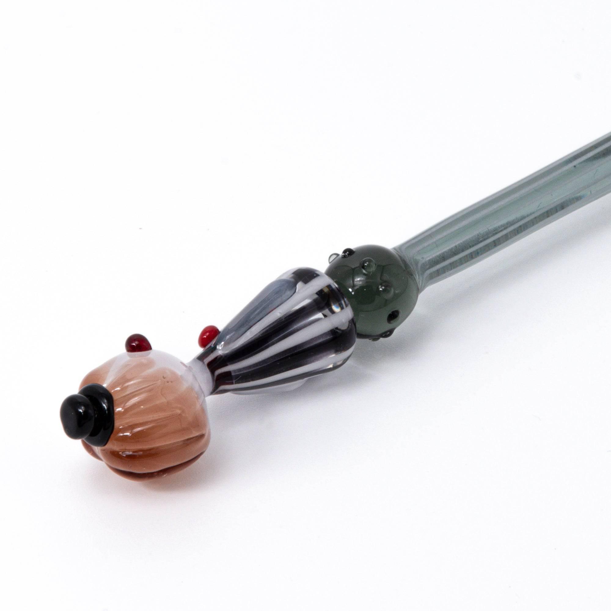 A striped glass dip pen with a whimsical lady figurine top, featuring elegant curves and handcrafted details.