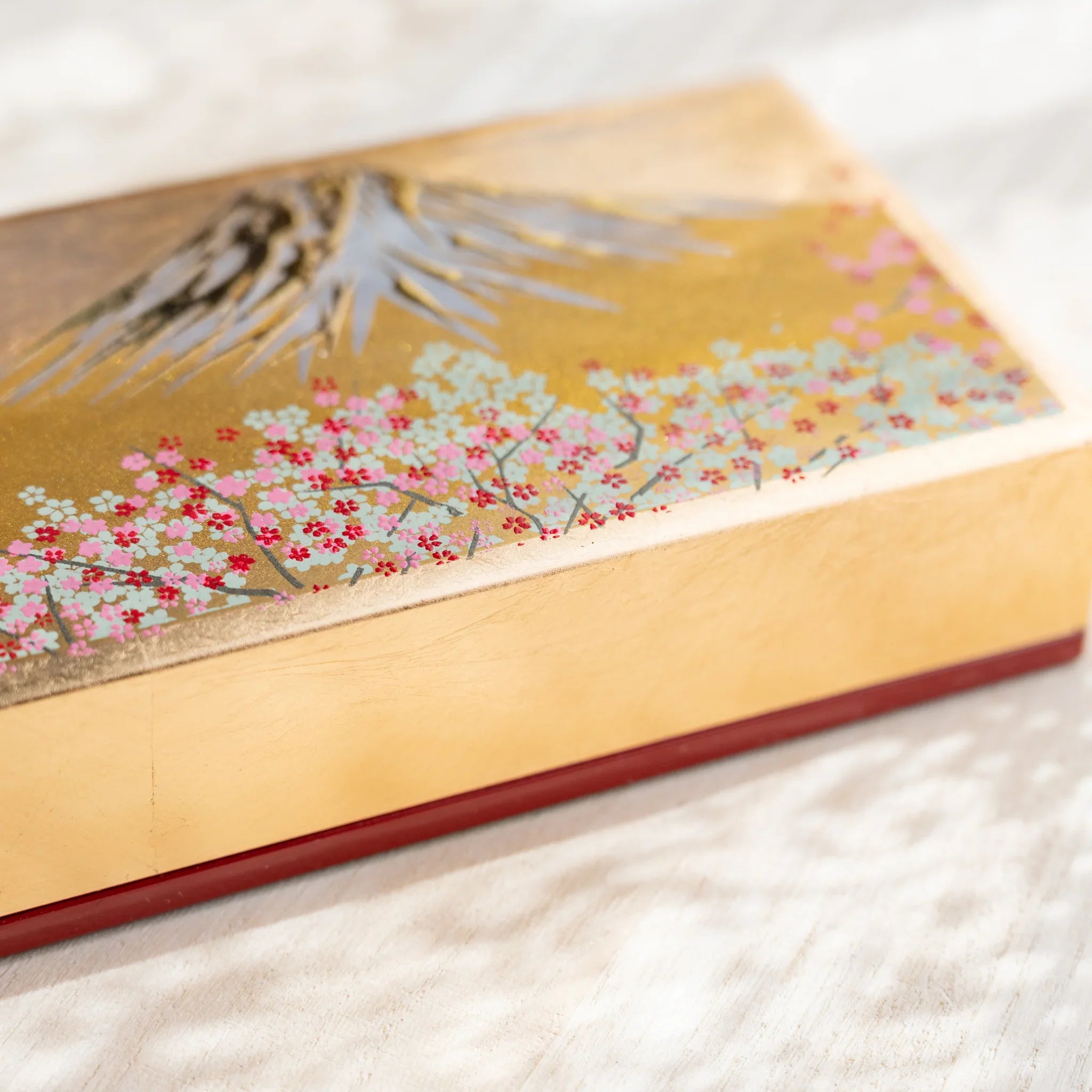 Close-up of golden Japanese pen case lid with silver pine and cherry blossom motifs showcasing Japanese art