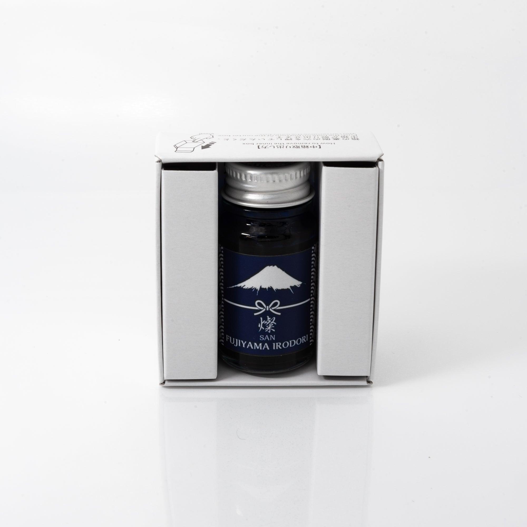 Open Fujiyama Irodori-san ink bottle with a vivid blue liquid, placed beside a fountain pen on a desk, emphasizing functionality and elegance.