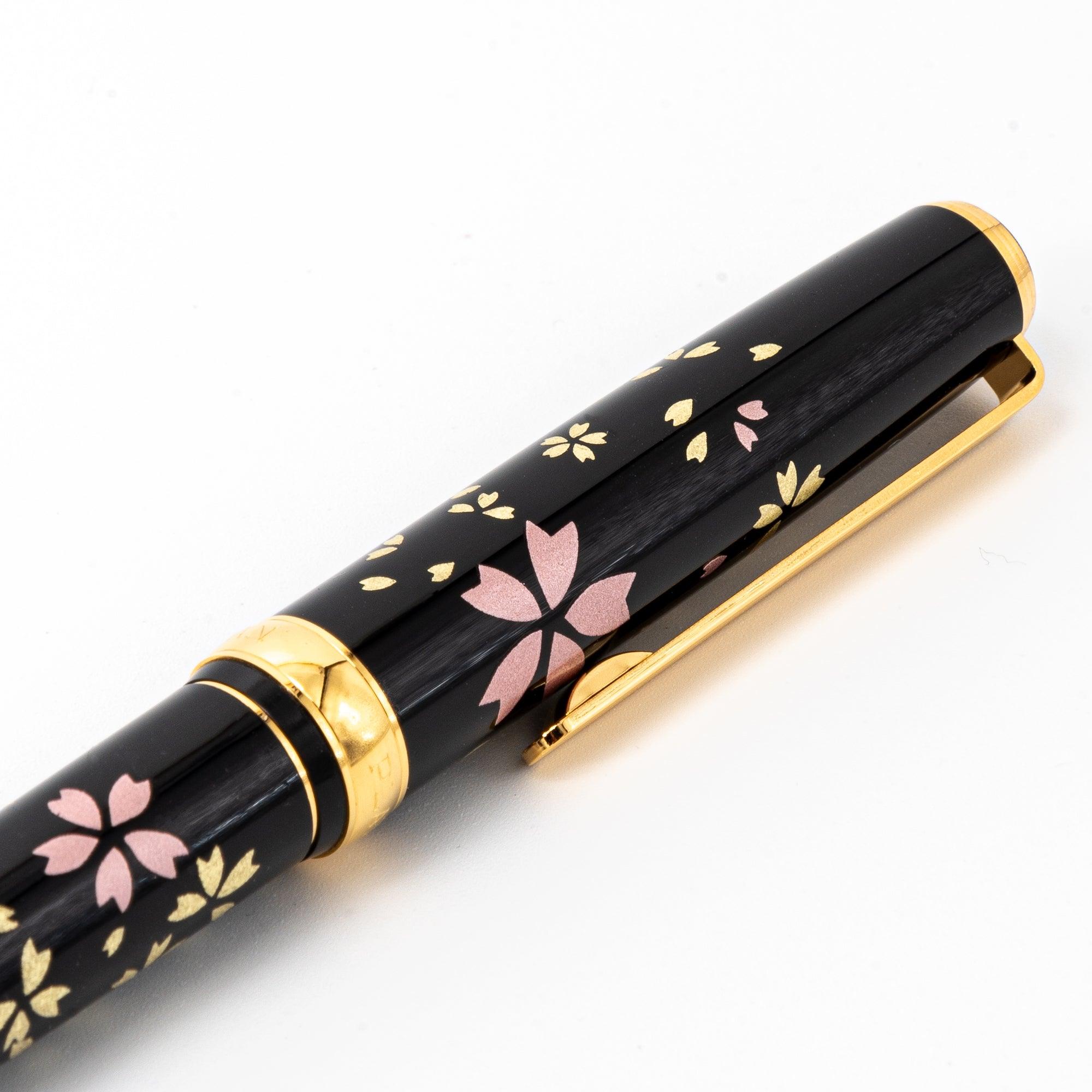 Close-up of a Japanese fountain pen’s black lacquered cap, detailed with gold and pink sakura motifs, highlighting its intricate artisanal design.