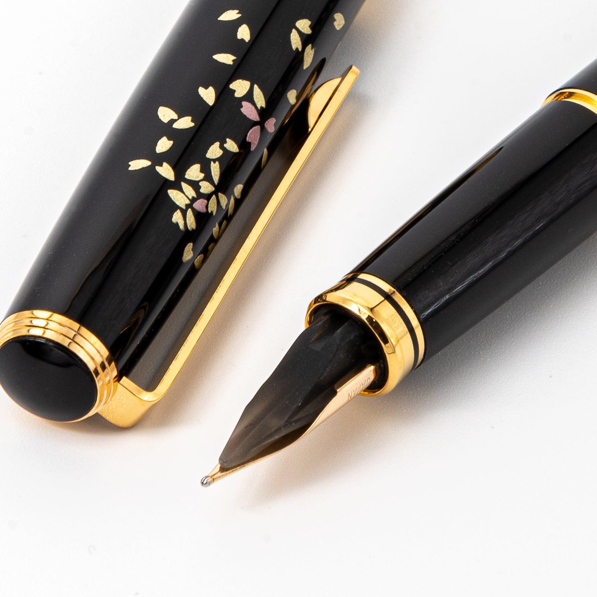 Elegant Japanese fountain pen with sakura motifs, intricate gold and pink floral patterns, gold accents, showcased with cap detail. (124文字)  