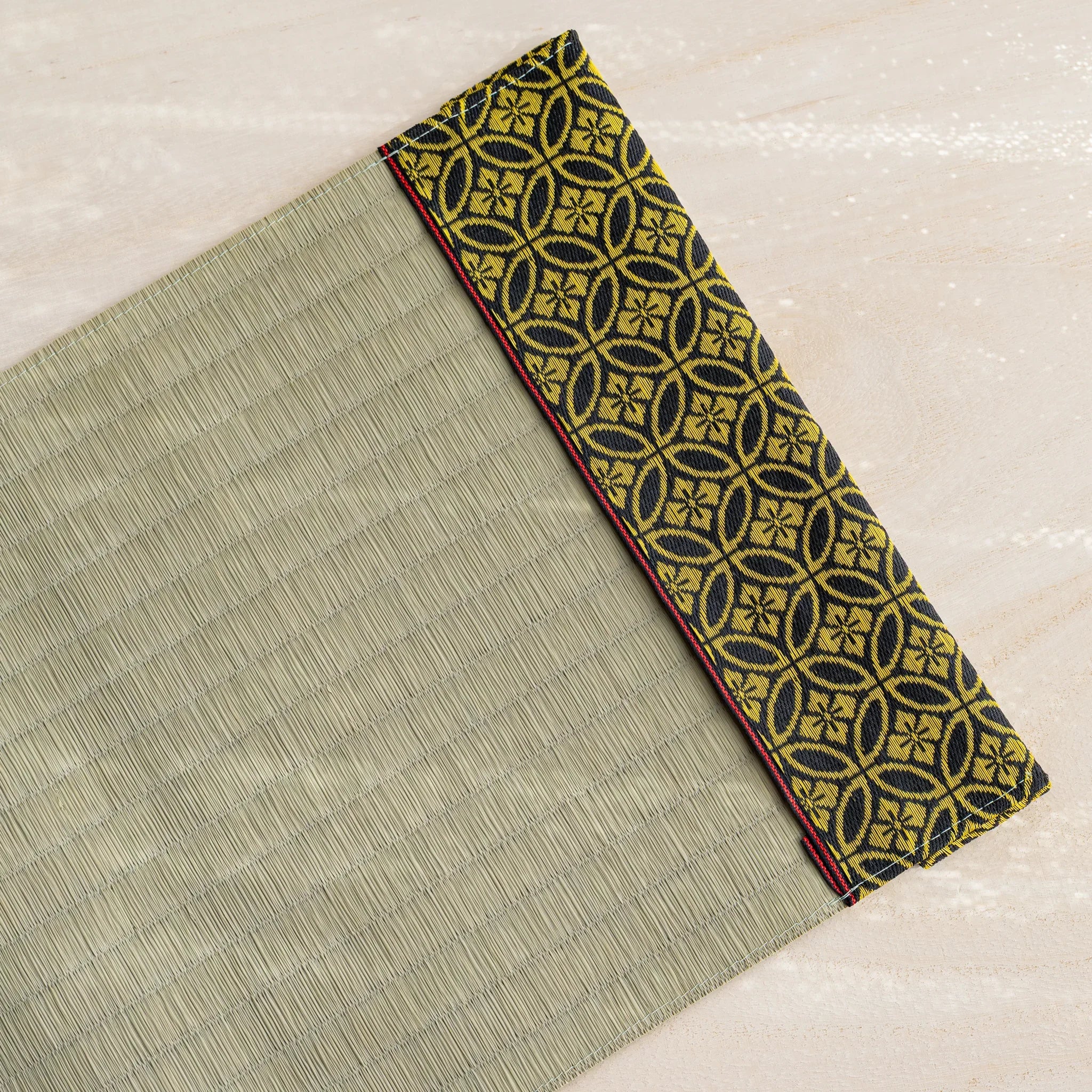 Angled view of Gold Shippo tatami book cover, green rush straw beside black and gold fabric band with red stitched edge