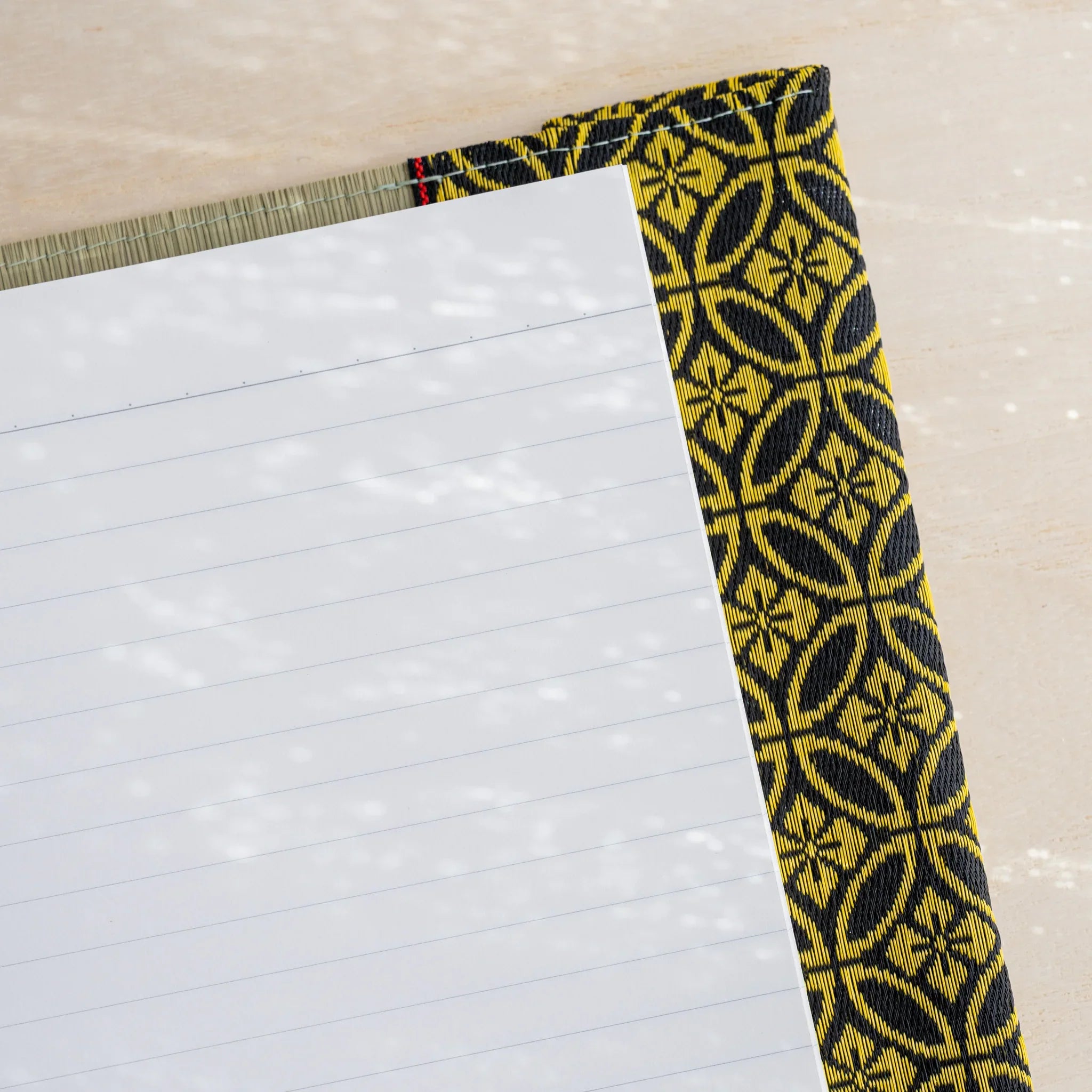 Corner close-up of white lined notebook page inside tatami cover with black and gold Japanese shippo circle flap