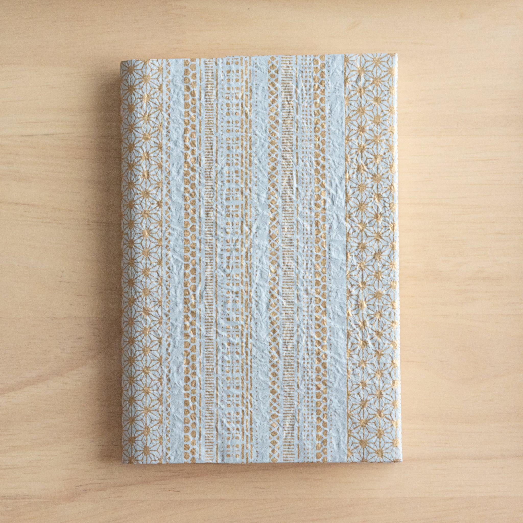 A notebook with a blue and gold striped pattern featuring intricate details, placed on a light wooden surface.