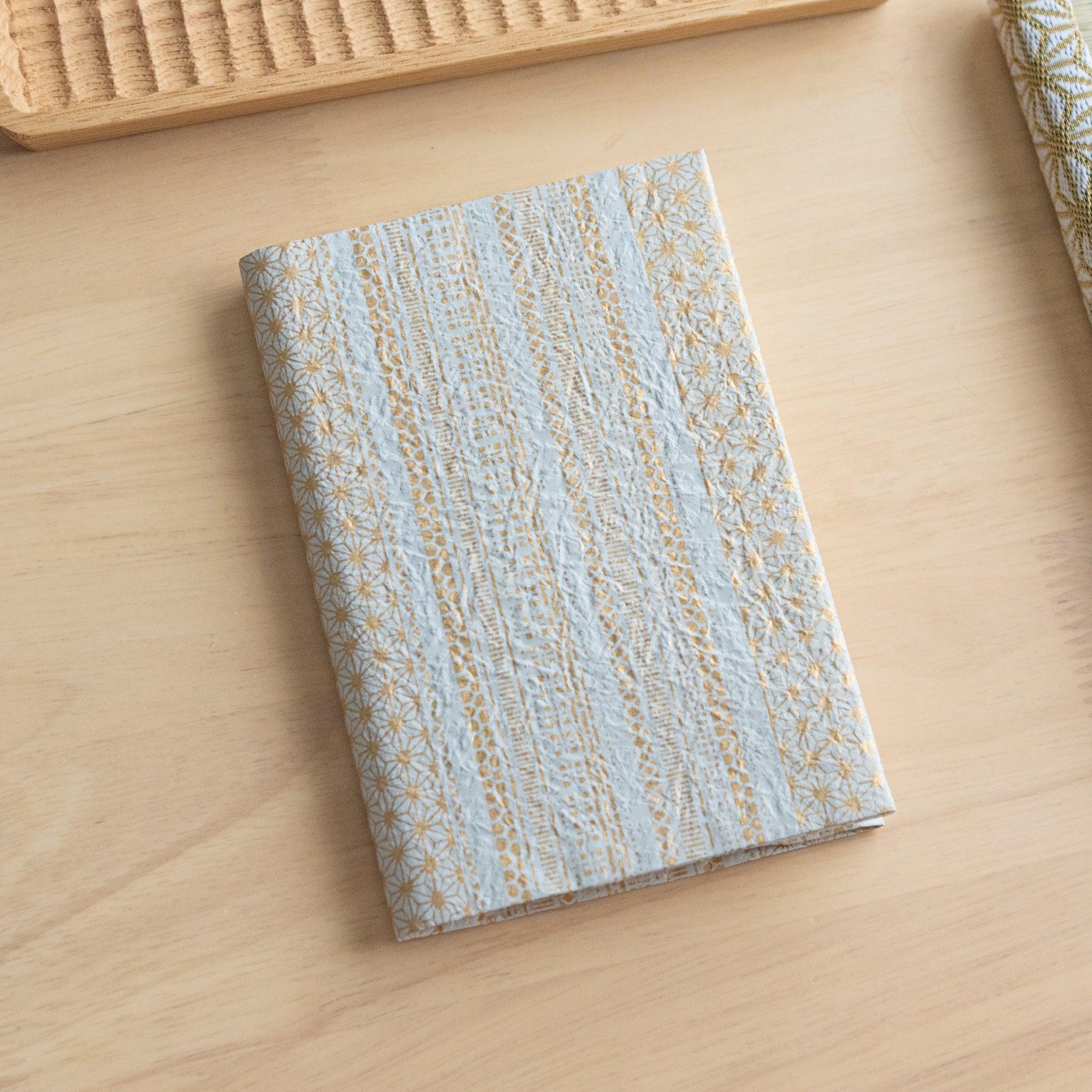 A notebook with a blue and gold patterned cover featuring intricate details, placed on a light wooden surface.