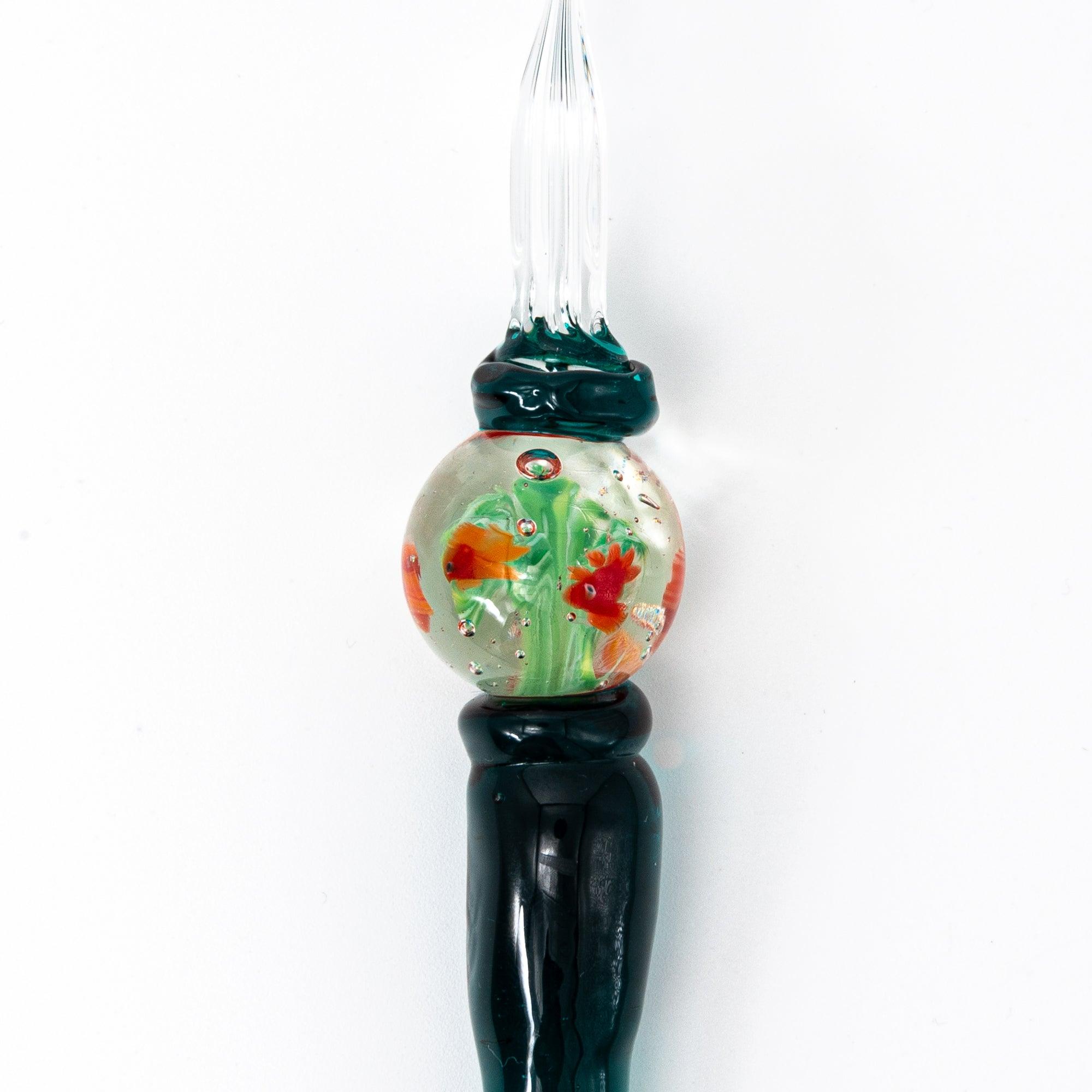 Side view of glass pen with goldfish motif encased like a fishbowl, featuring dark green handle.