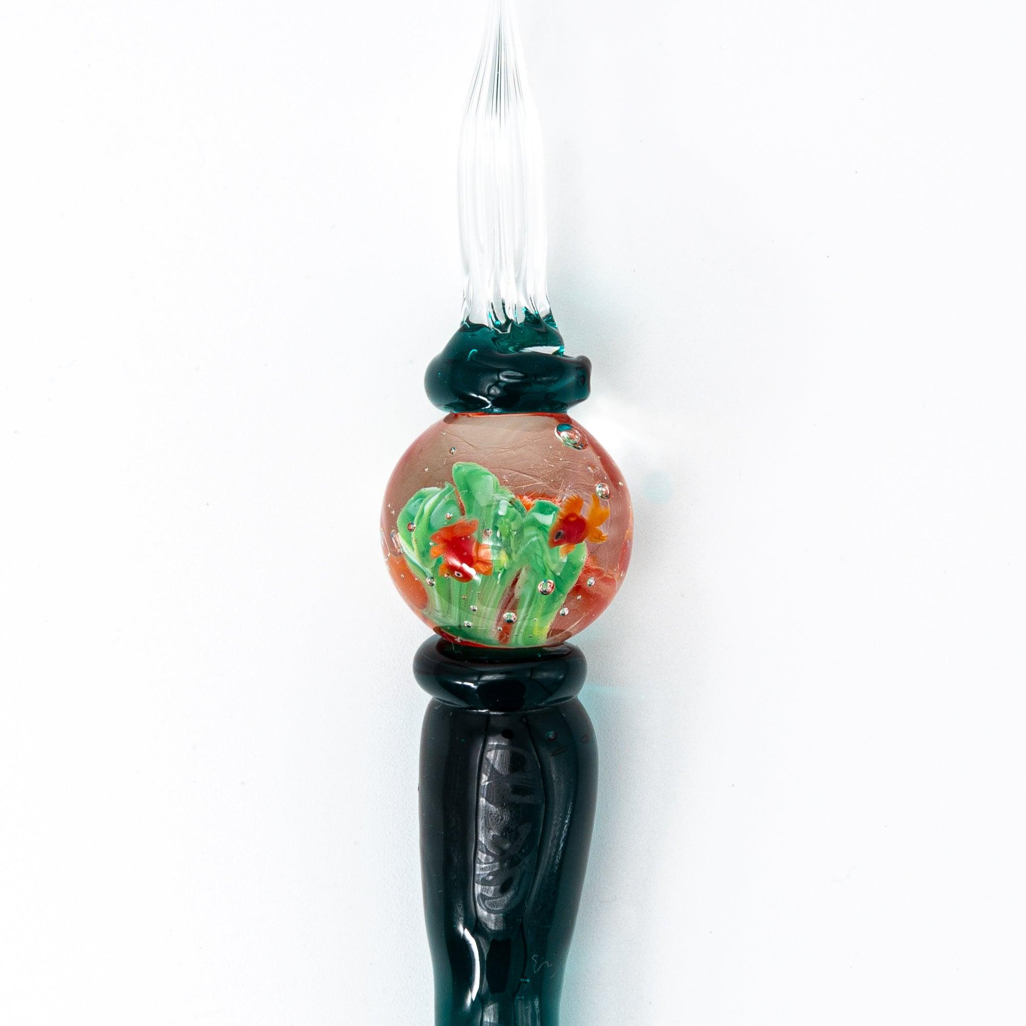 Side view of glass pen with goldfish motif encased like a fishbowl, featuring dark green handle.