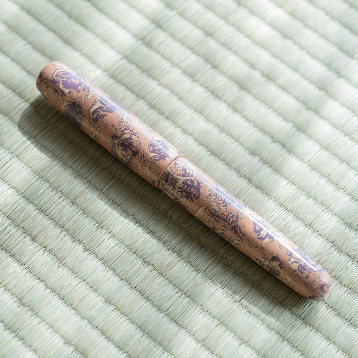 Capped Hanagasumi Tsugaru-nuri fountain pen lying diagonally on tatami in sunlight, pink and purple urushi