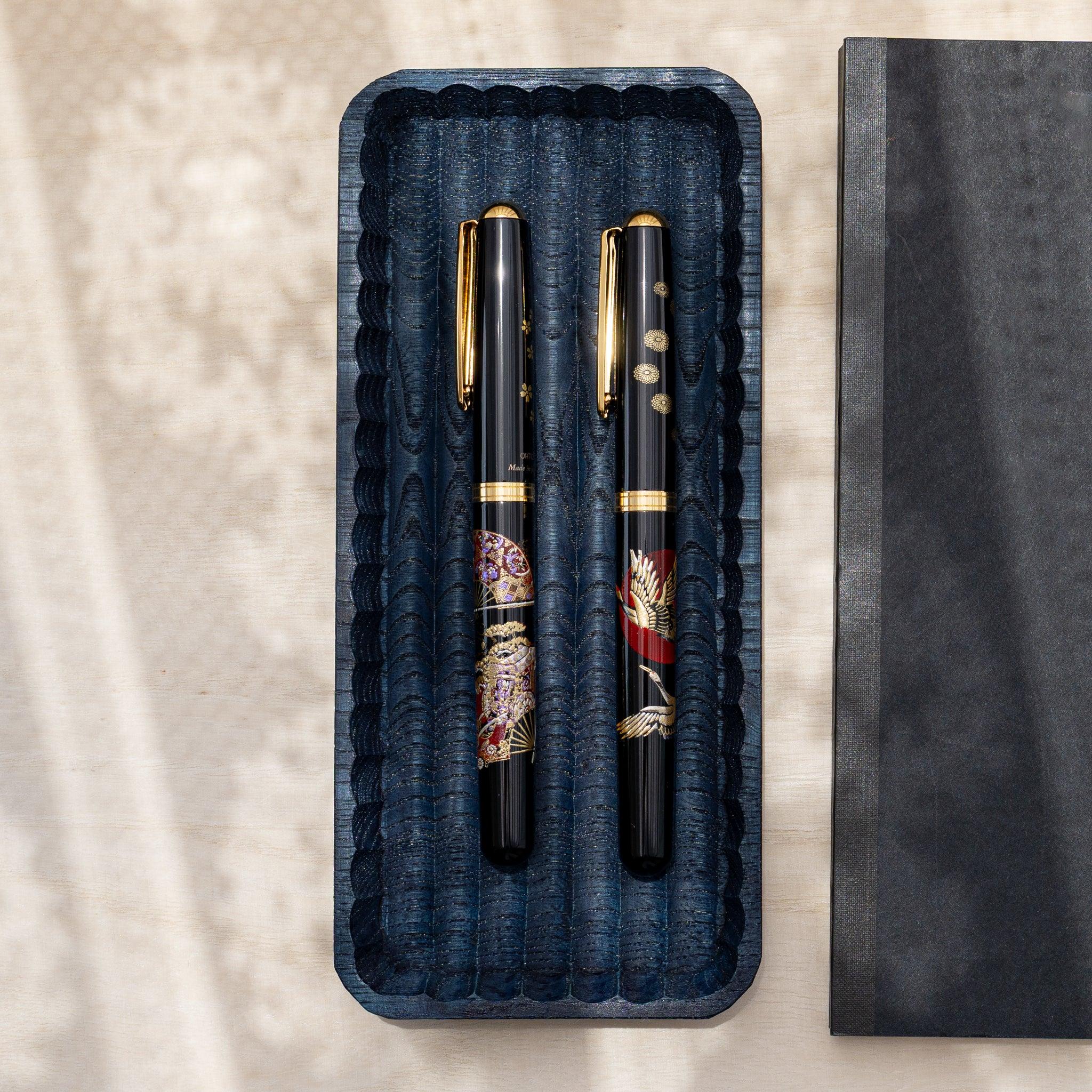 Indigo dyed slim chestnut pen tray from above holding two black fountain pens with gold crane and fan designs