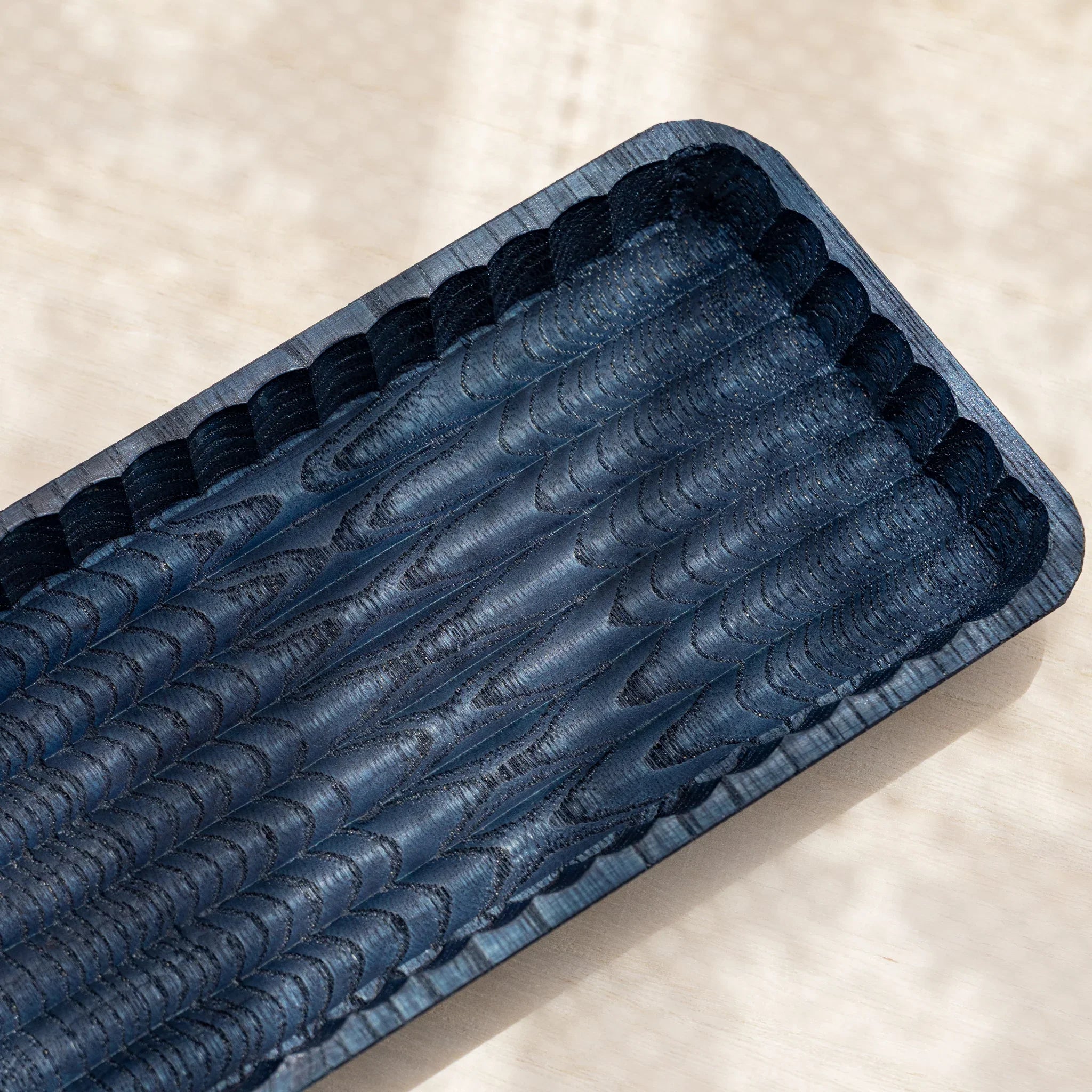 Close-up of indigo dyed slim pen tray showing overlapping chisel-carved scallops inside the tray and along the rim